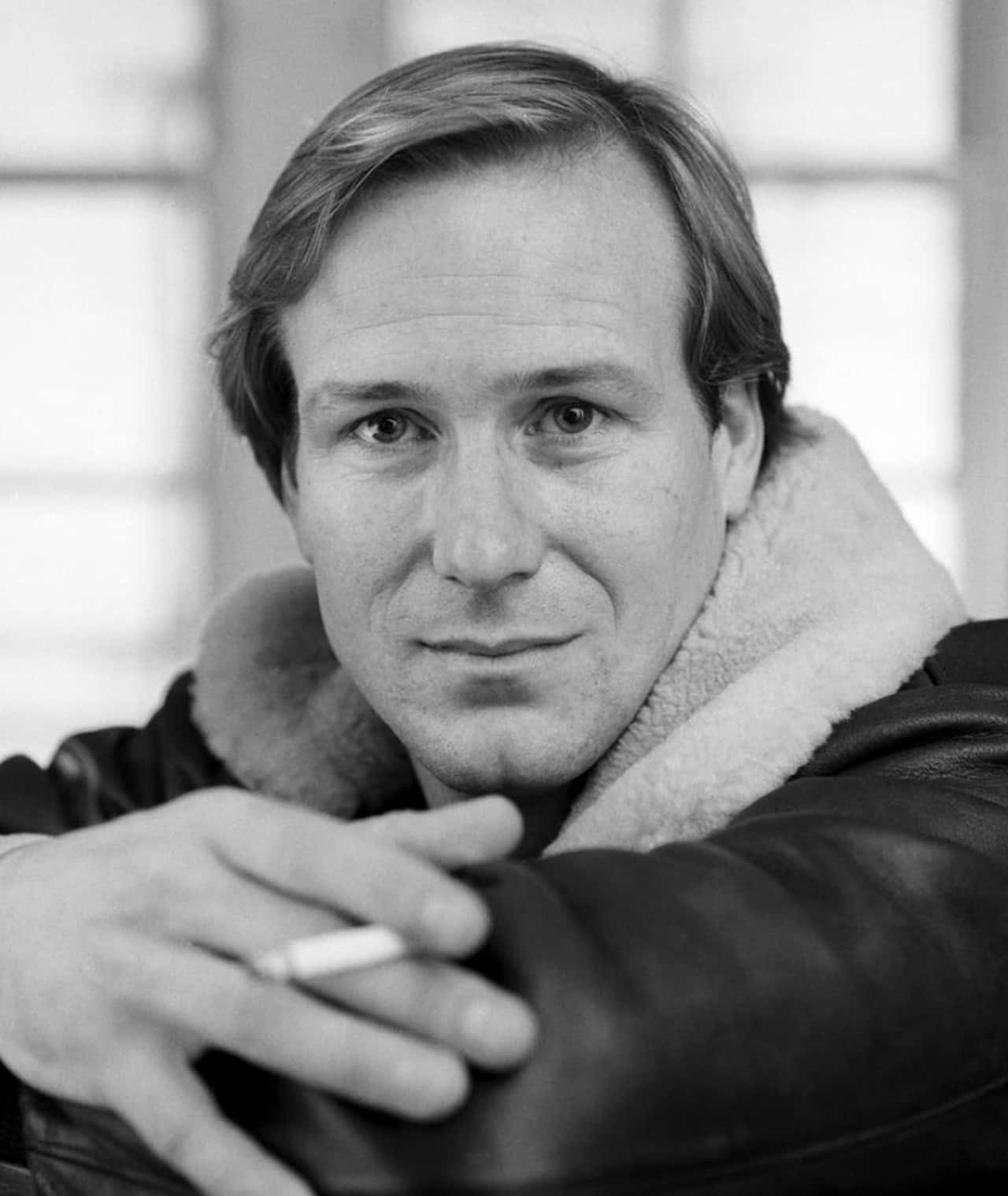 William Hurt 桌布 壁紙 — 一個穿著羊羔毛領外套的男人，手持香煙，神情平靜的黑白肖像。