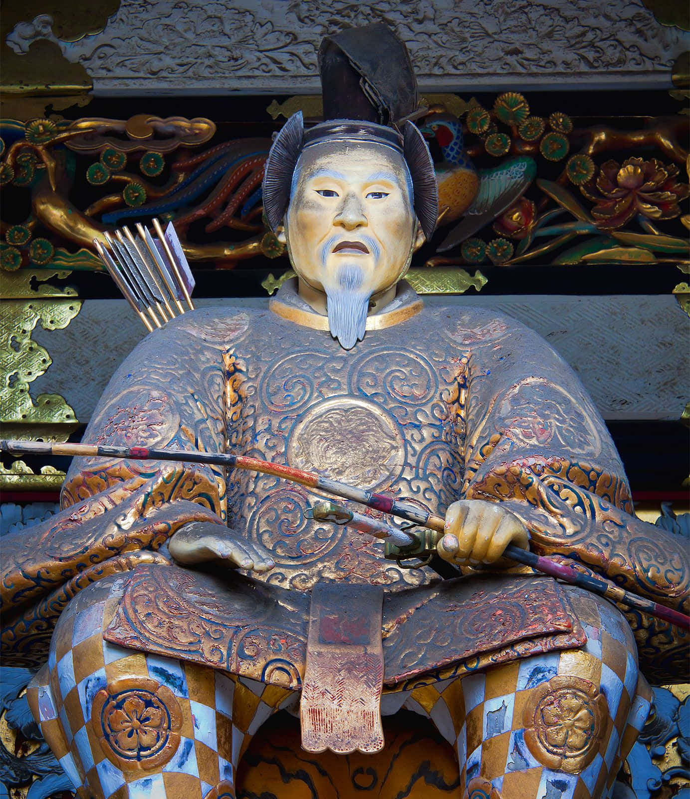 Tokugawa 桌布 壁紙 — 一個穿著華麗盔甲、手持弓箭的武士戰士的詳細木雕，坐在鍍金神社外牆下方。