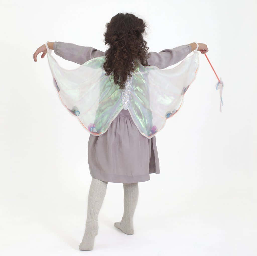 Butterfly Wing Dress 桌布 壁紙 — 一個穿著薰衣草色連衣裙和銀色虹彩仙子翅膀的孩子，在純白色背景前張開雙臂站立。