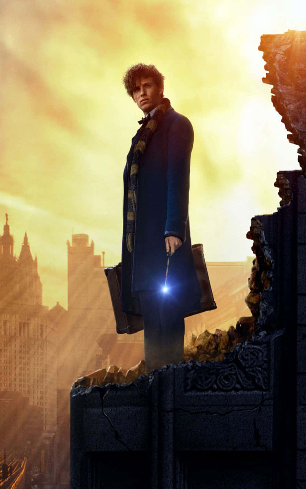 Fantastic Beasts 桌布 壁紙 — 一個穿著藍色外套的男人站在破碎的石頭結構上，手持發光的魔杖，背景是城市天際線上的金色日落。