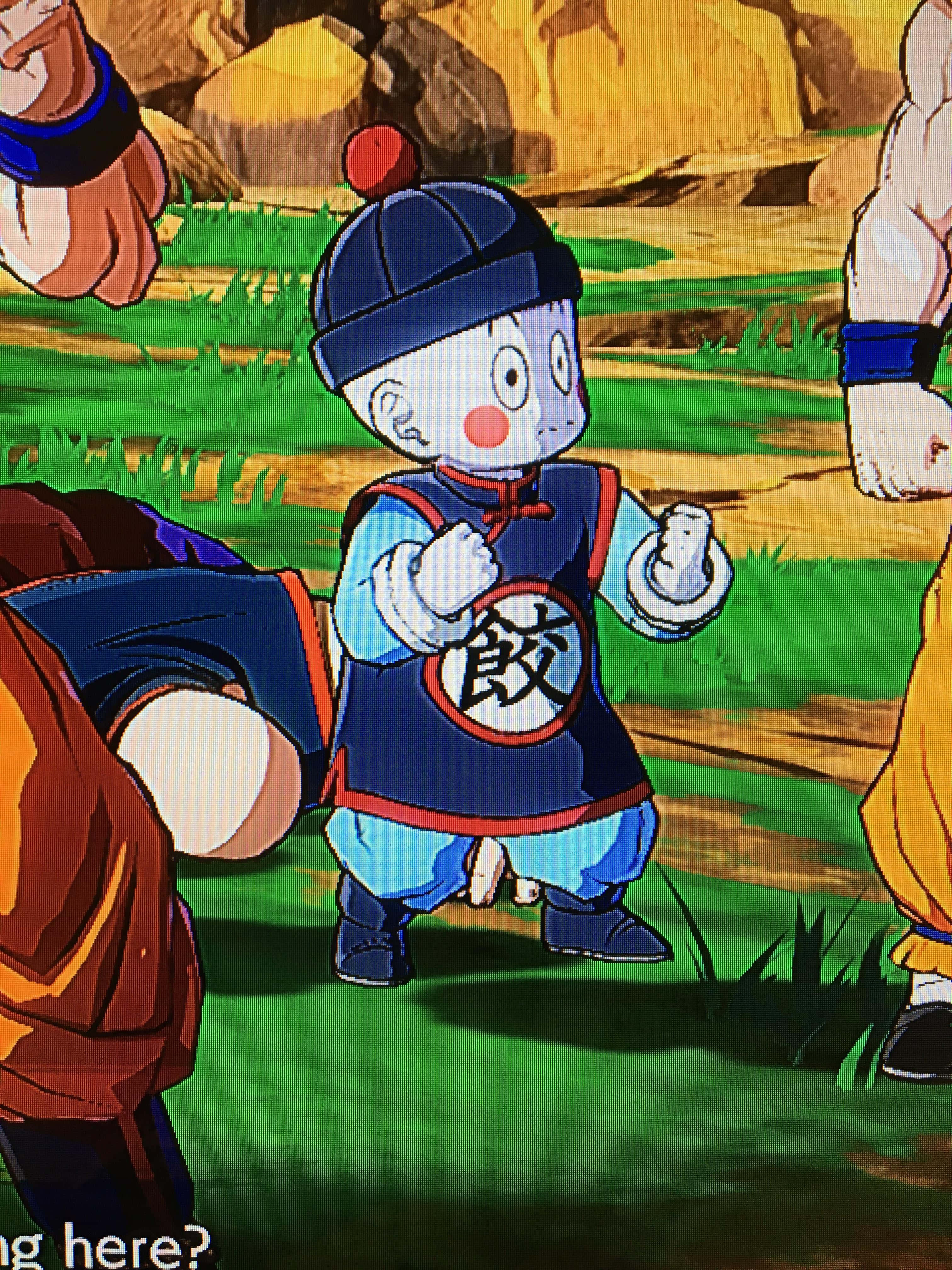 Chiaotzu 桌布 壁紙 — 一個穿著藍色武術裝備的小型動漫角色自信地站在一個有岩石地形的草地戶外場景中。
