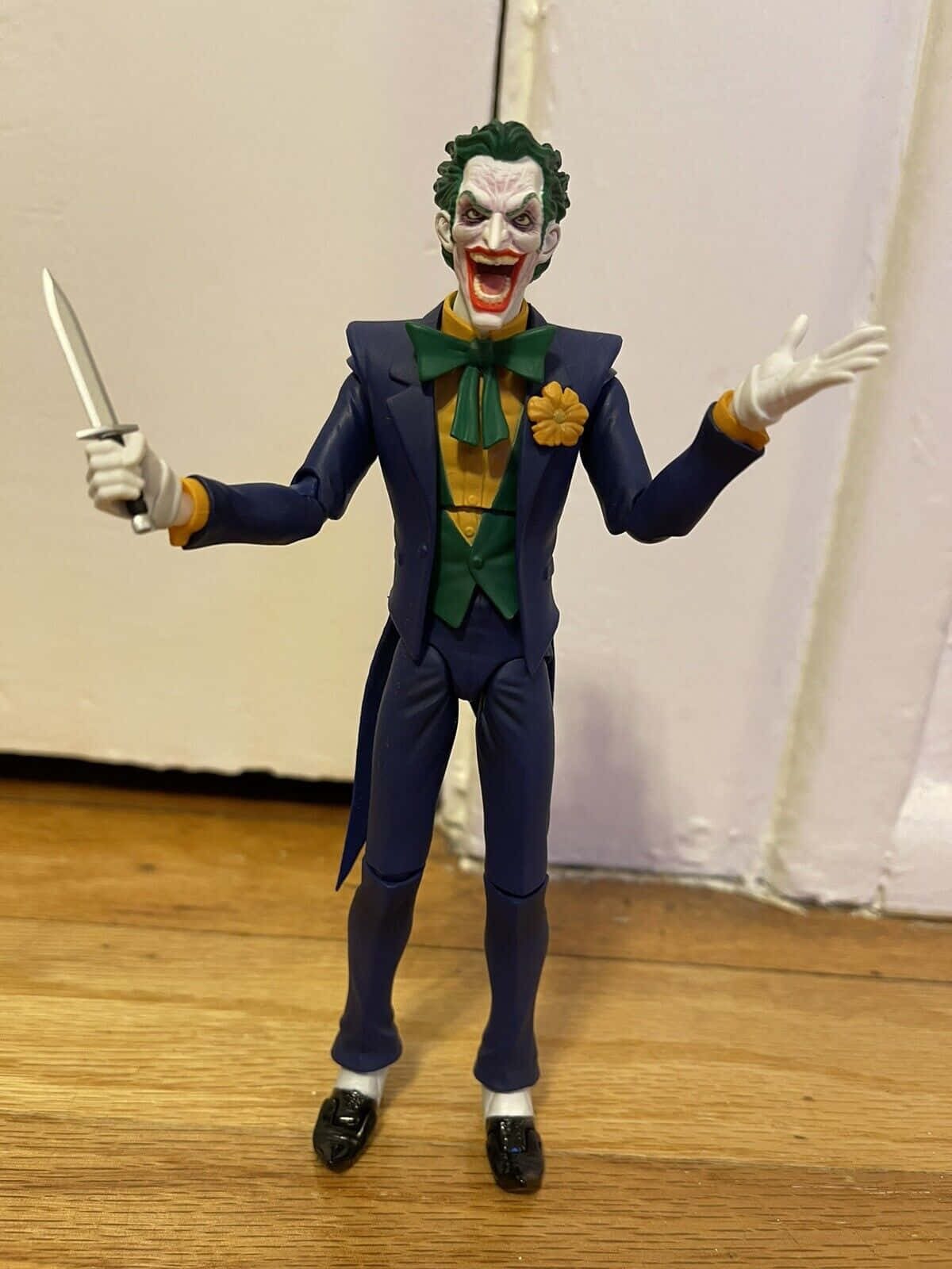 Batman Hush 桌布 壁紙 — 一個穿著藍色西裝和綠色蝴蝶結的小丑可動人偶站在木地板上，手持刀，露出狂笑。