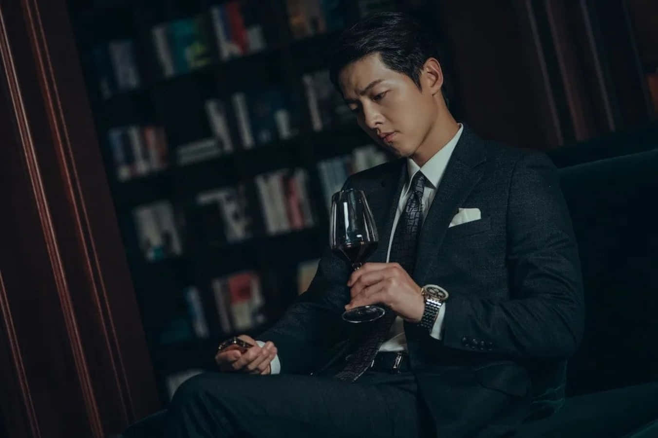 一個穿著西裝的男人坐在沙發上，手持酒杯 壁紙