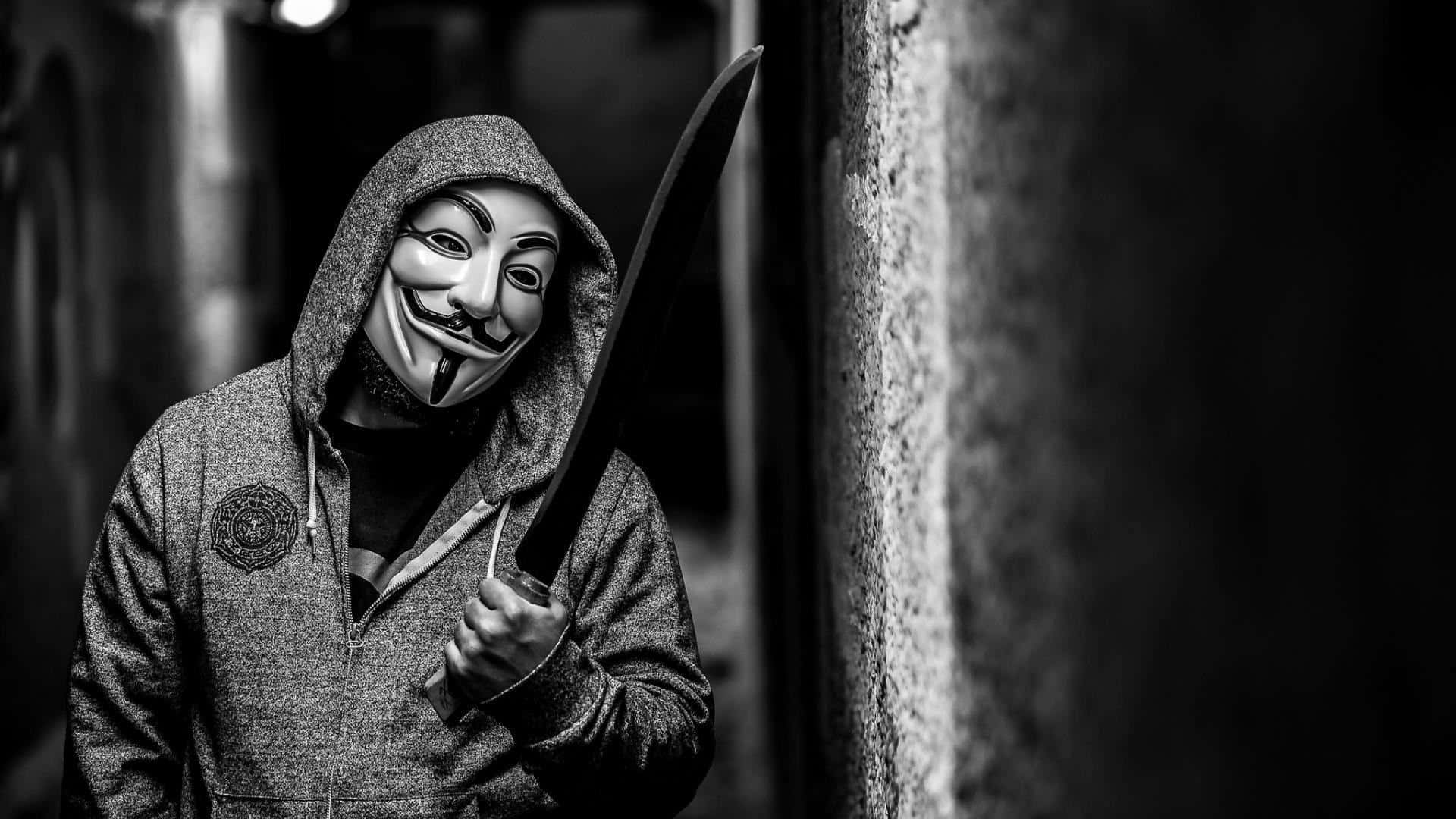 Anonymous 桌布 壁紙 — 一個穿著連帽衫和蓋伊·福克斯面具的人，在昏暗的小巷中手持一把大刀，黑白畫面。