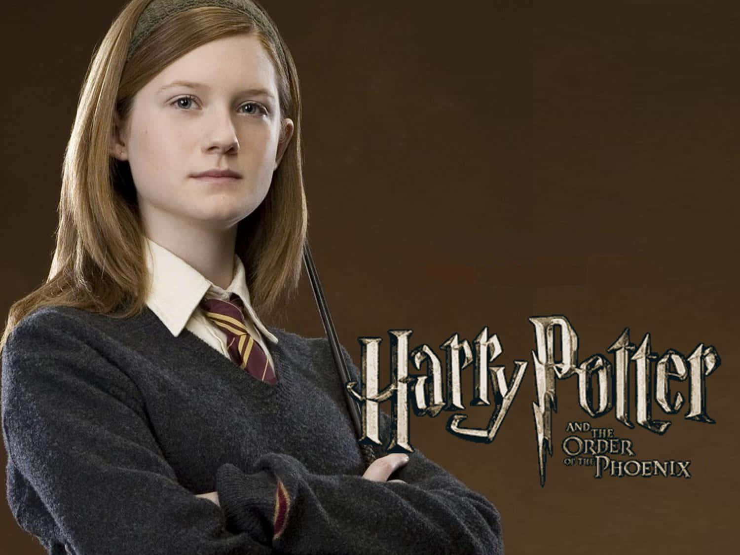 Ginny Weasley 桌布 壁紙 — 一個穿著霍格華茲制服嘅年輕女巫，喺啡色背景前自信地交叉雙臂，背景有《哈利波特：鳳凰會的密令》嘅標題。