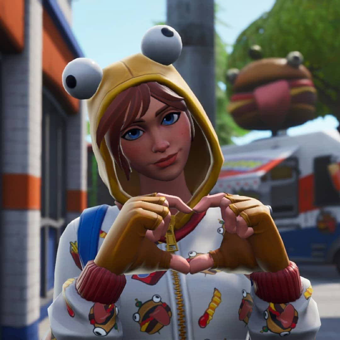 遊戲 桌布 壁紙 — 一個穿著黃色青蛙連帽衫的Fortnite角色在陽光明媚的城市背景下用手比出心形。