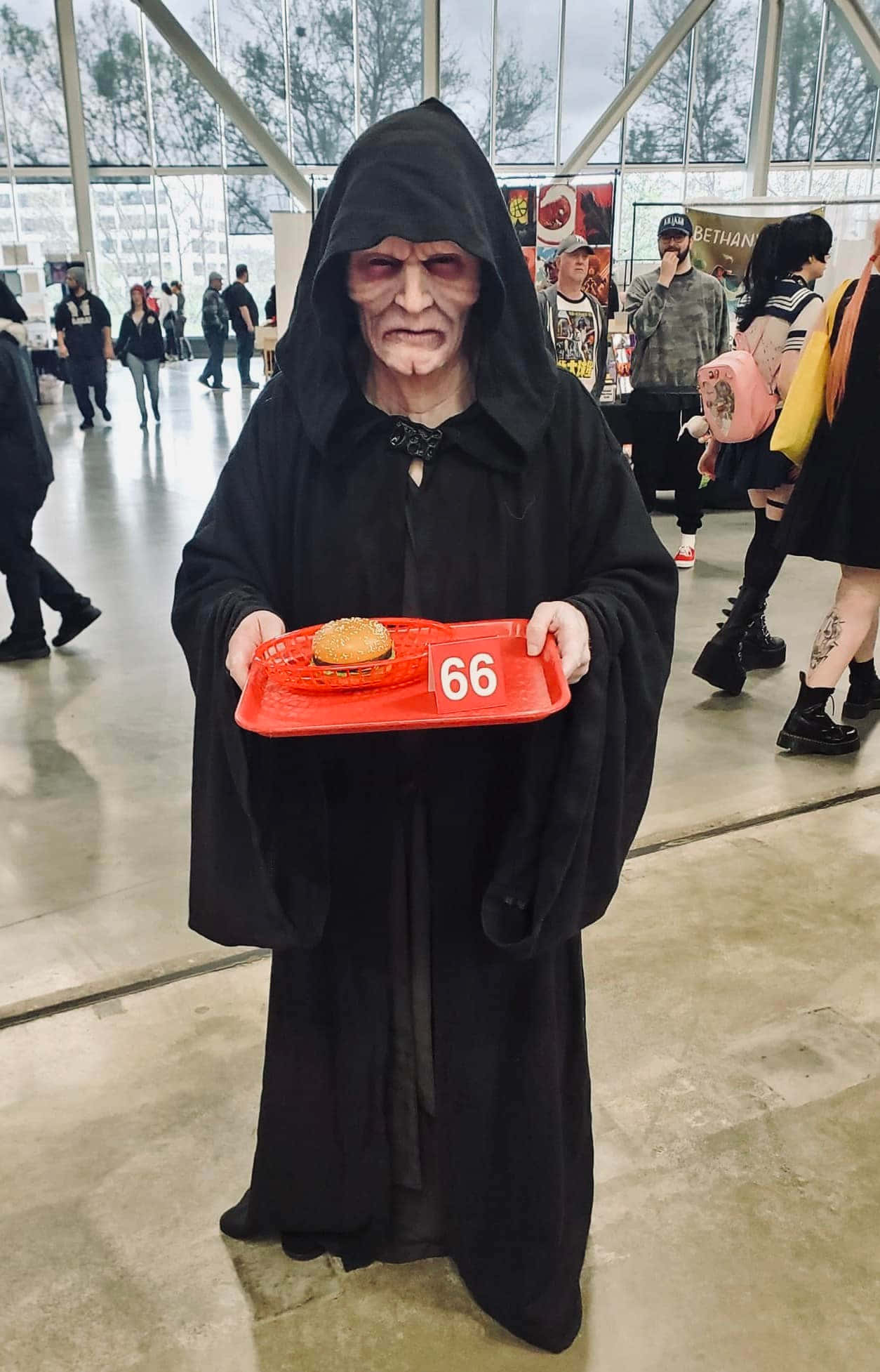 The Order 66 桌布 壁紙 — 一個穿著黑武士服裝的人喺展會上拎住一個紅色托盤，上面有一個漢堡同數字66。
