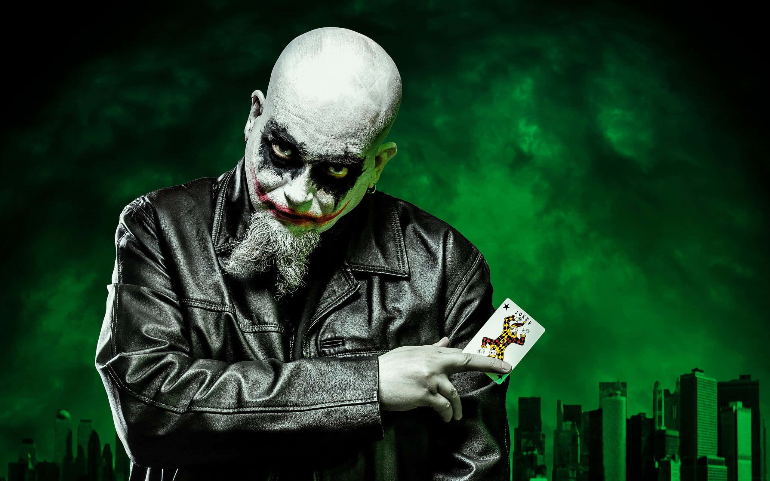 Evil Joker 桌布 壁紙 — 一個穿著黑色皮褸的威脅性小丑，在發光的綠色城市景觀背景下拿著一張小丑牌。