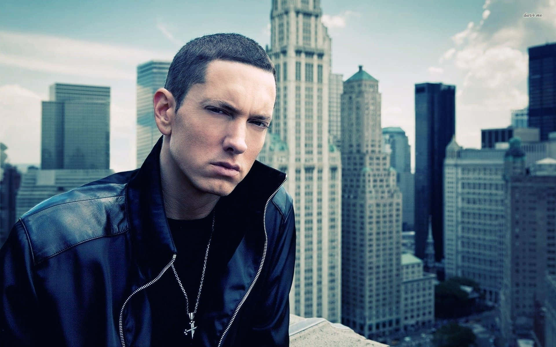Eminem 桌布 壁紙 — 一個穿著黑色皮褸的男人站在天台，俯瞰著陰雲密佈的天空下高聳的城市天際線。