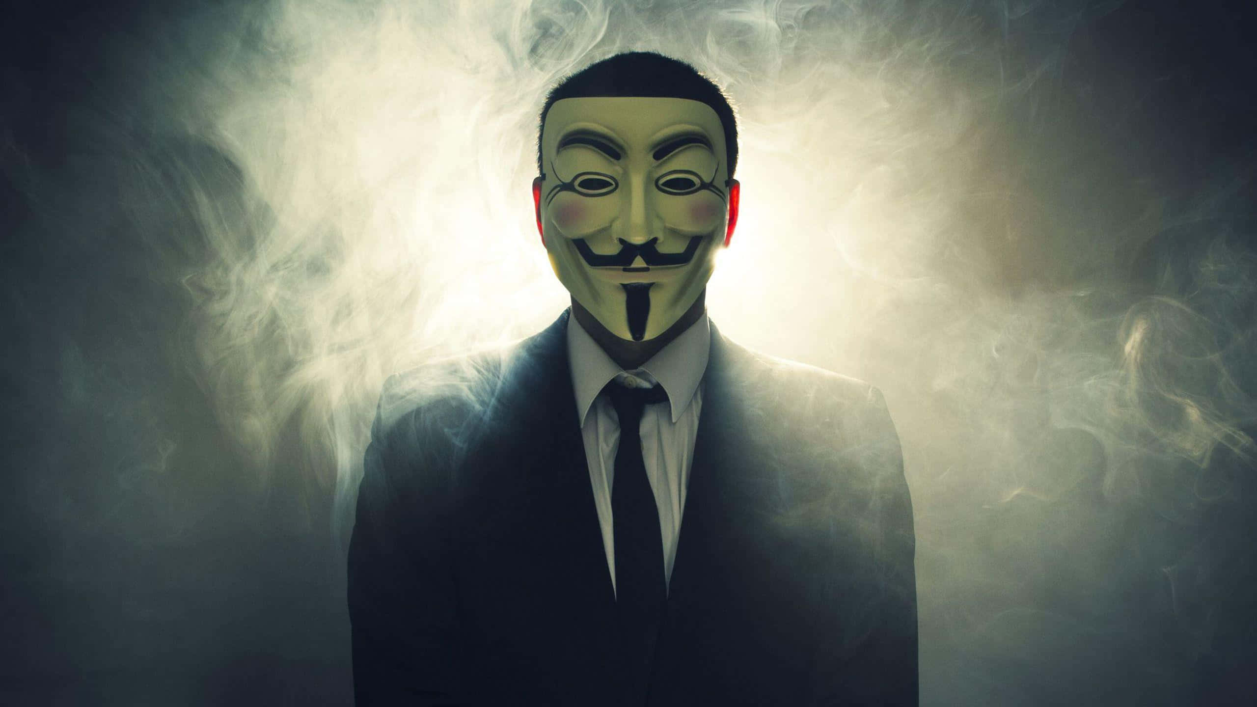 Anonymous 桌布 壁紙 — 一個穿著黑色西裝、戴著標誌性綠色蓋伊·福克斯面具的人，在旋轉的煙霧中背光而立。