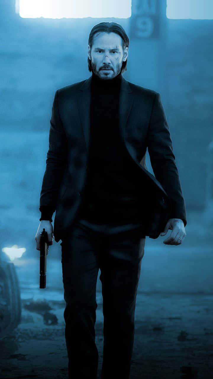 Keanu Reeves 桌布 壁紙 — 一個穿著黑色西裝的男人在藍色調的工業天空下持槍向前走。