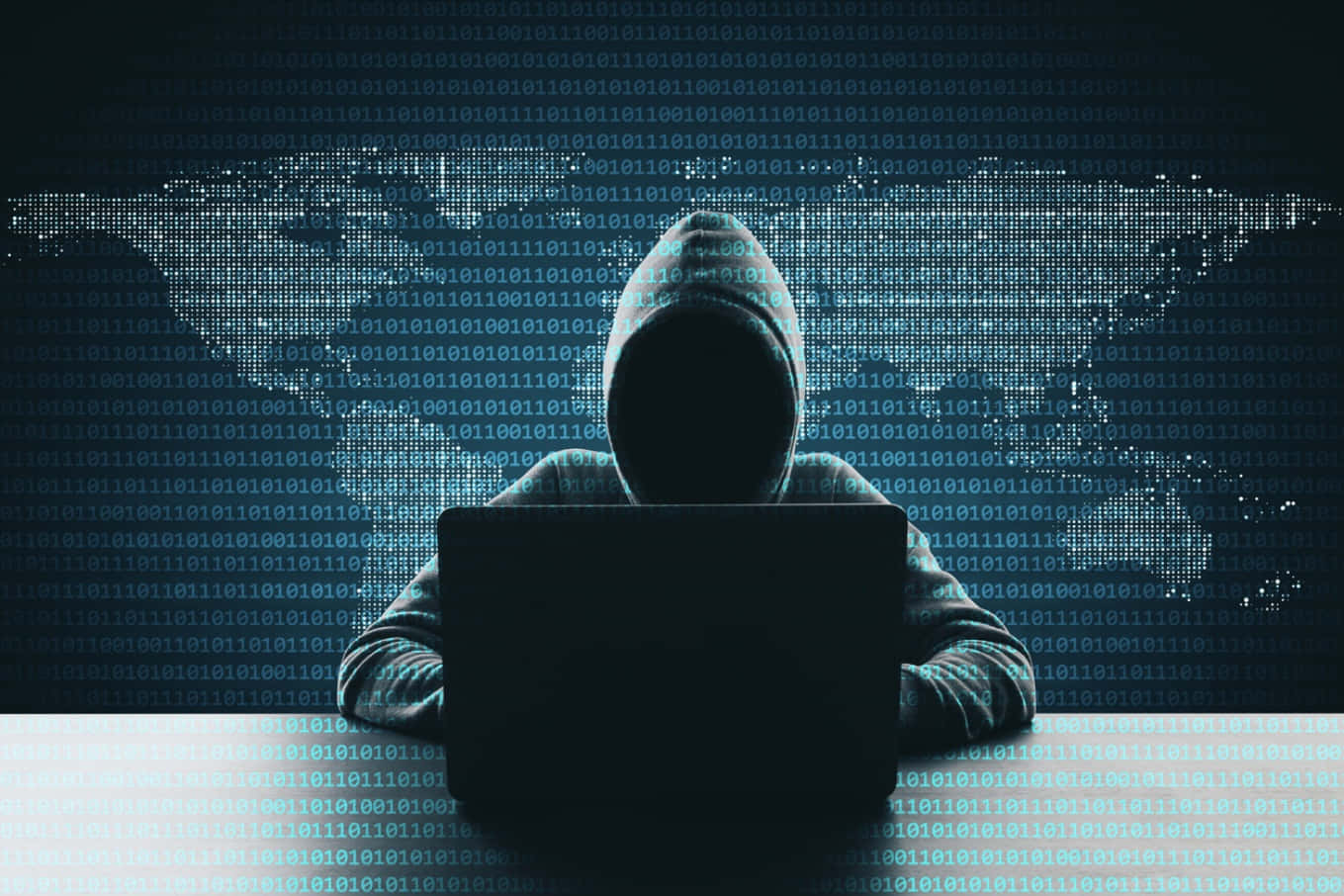 一個穿連帽衛衣的男人坐在書桌前用筆記本電腦 壁紙