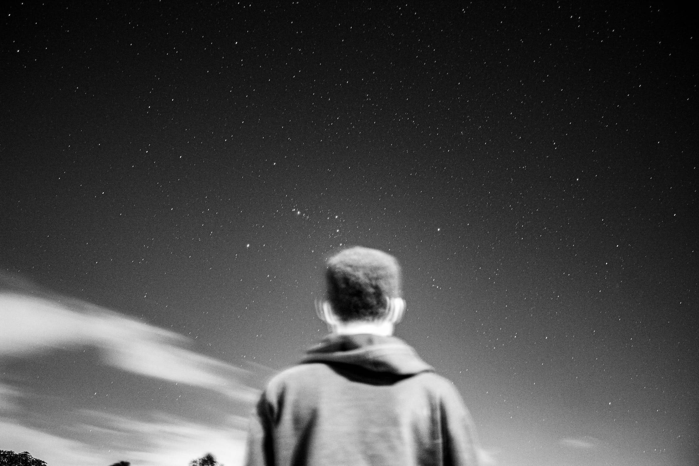 星星 桌布 壁紙 — 一個穿連帽衫的人仰望星空，下方有流動的雲層。