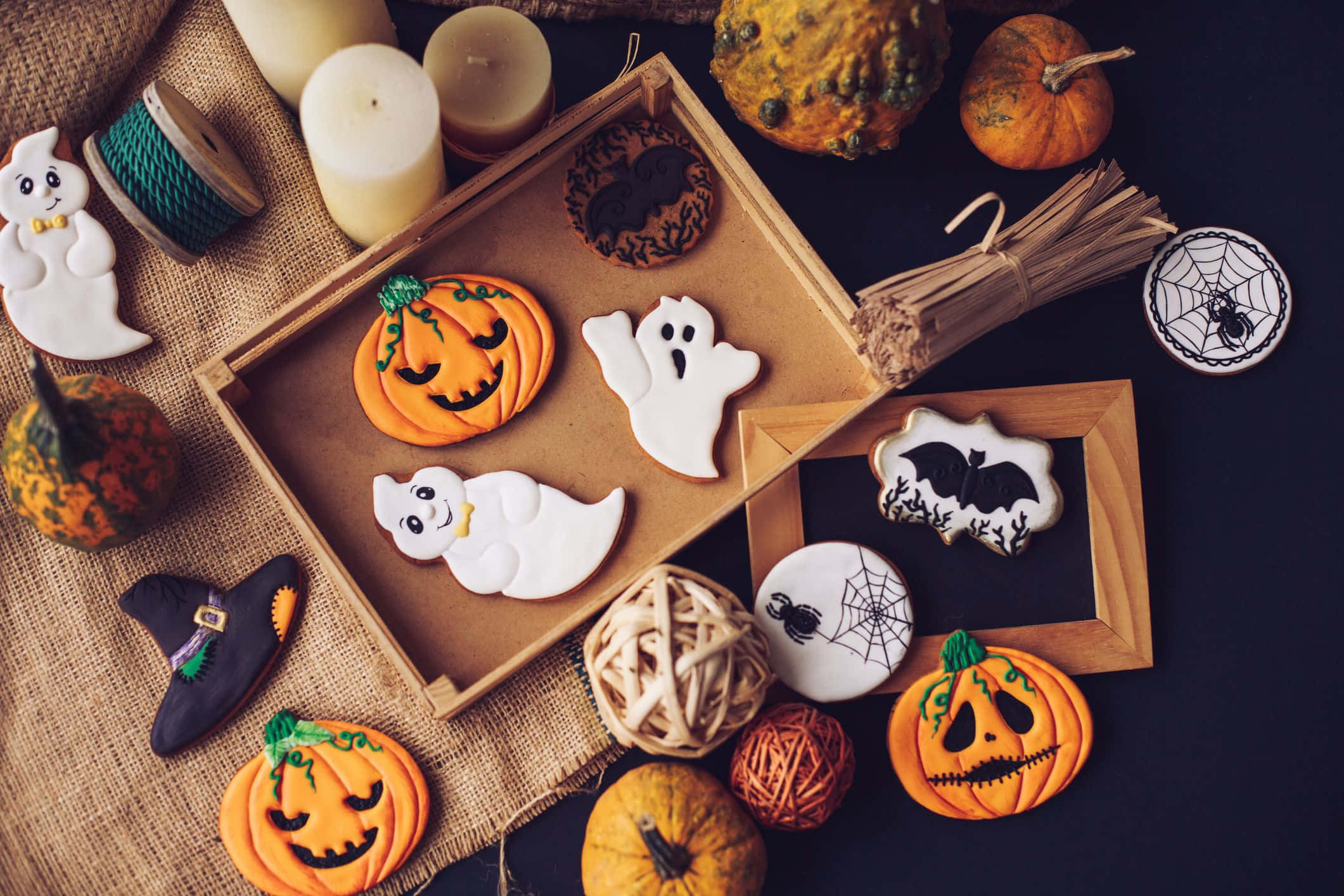 Halloween Treats 桌布 壁紙 — 一個節日氣氛的萬聖節擺設，包括傑克南瓜燈和鬼魂曲奇、南瓜、蠟燭和麻布上的蜘蛛網裝飾。