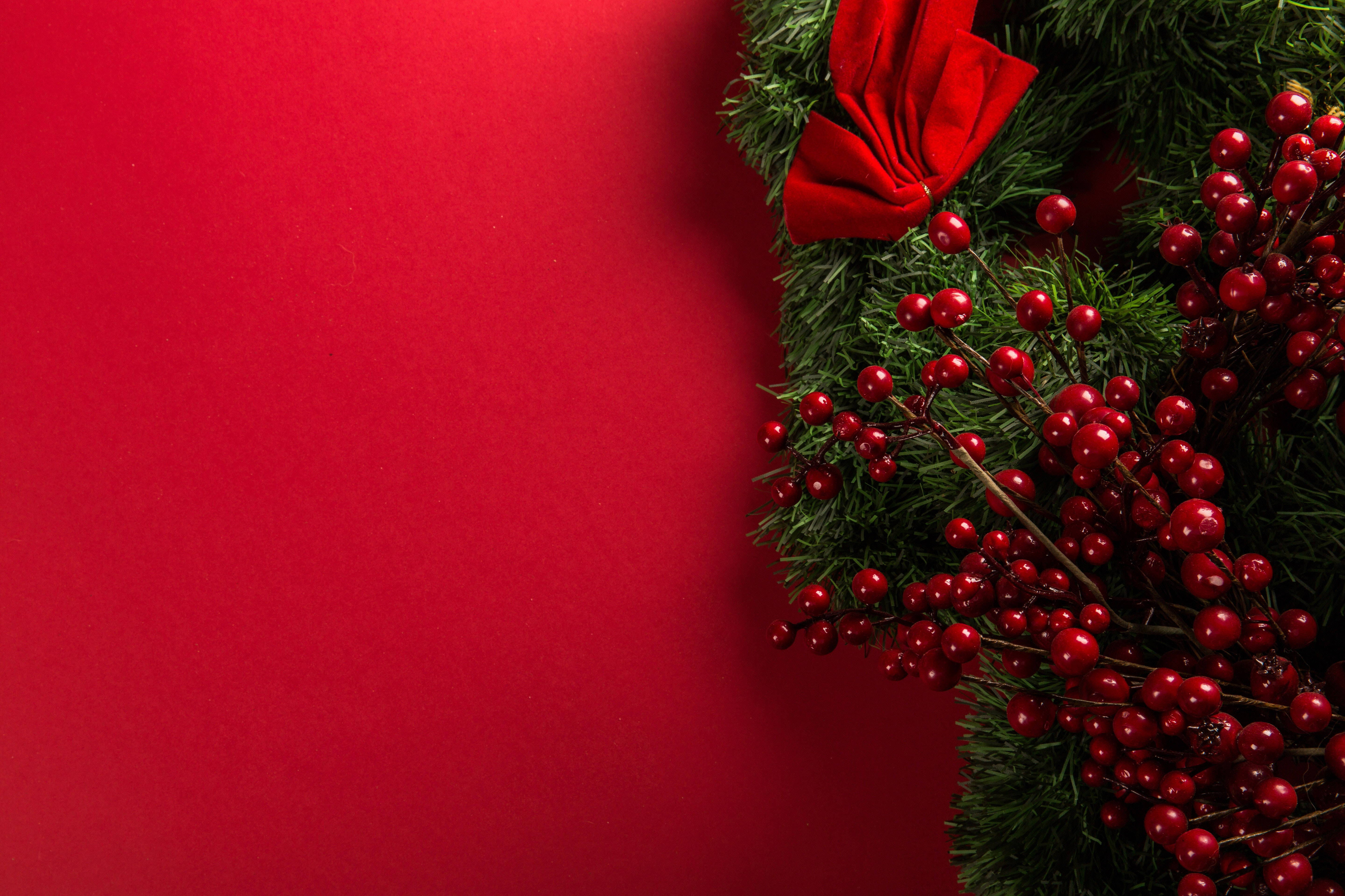 Christmas Wreath 桌布 壁紙 — 一個節日花環，帶有紅色漿果和蝴蝶結，放置在純紅色背景上。