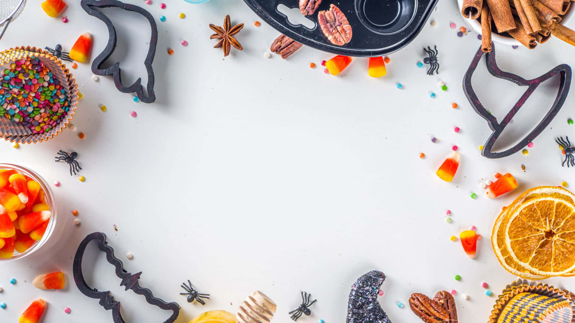 Halloween Cookie Cutters 桌布 壁紙 — 一個節日萬聖節平面擺設，以糖果玉米餅乾模具、乾橙片和糖針圍繞一個空白白色中心排列。