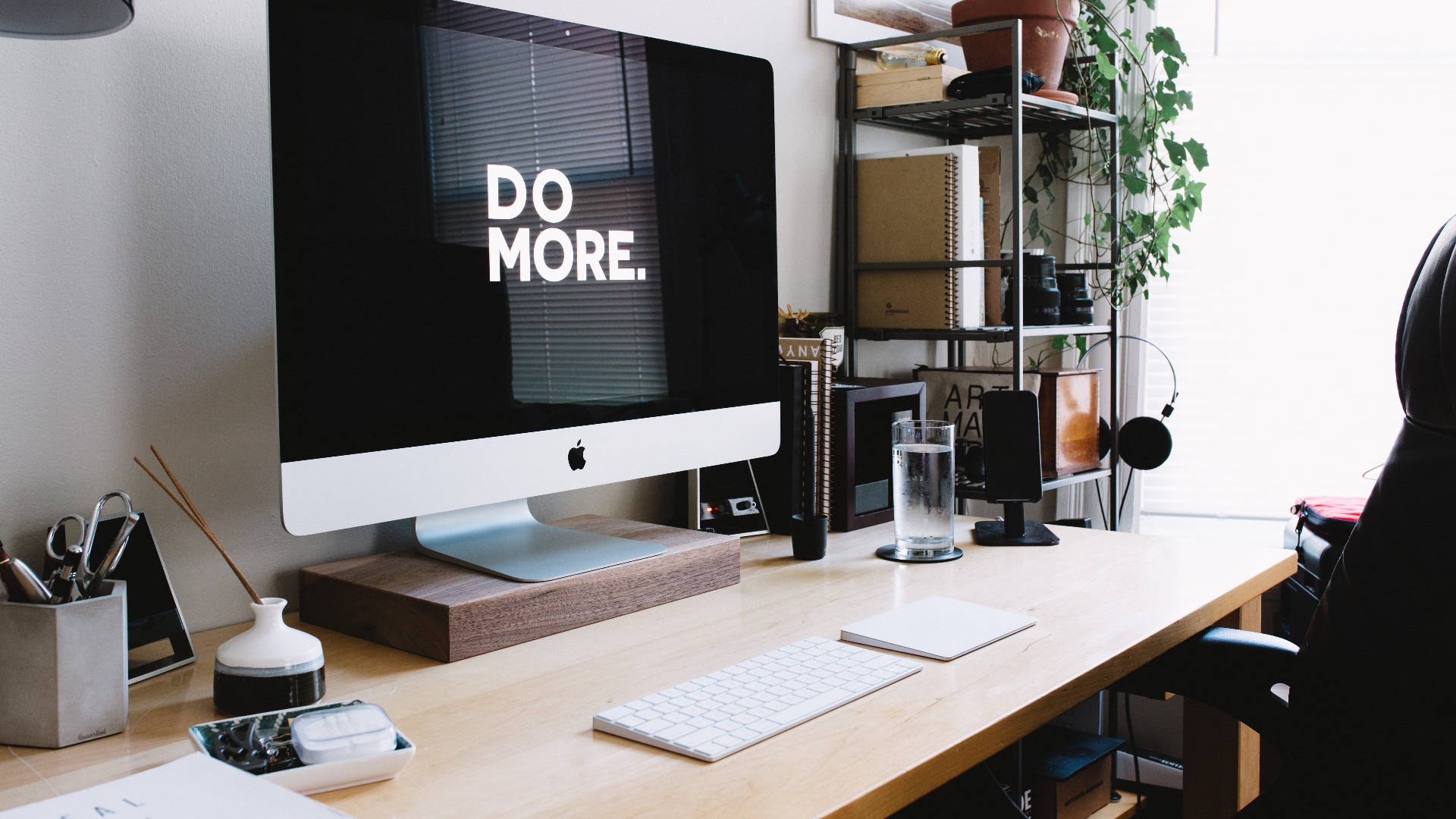 Working From Home 桌布 壁紙 — 一個簡約的家居辦公桌，配備時尚的iMac顯示'DO MORE.'，周圍環繞植物和現代科技。