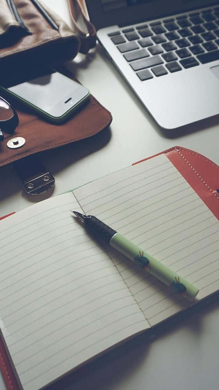 Diary 桌布 壁紙 — 一個簡約的工作空間，筆記本、筆、手提電腦和電話整齊地擺放在潔白的桌子上。