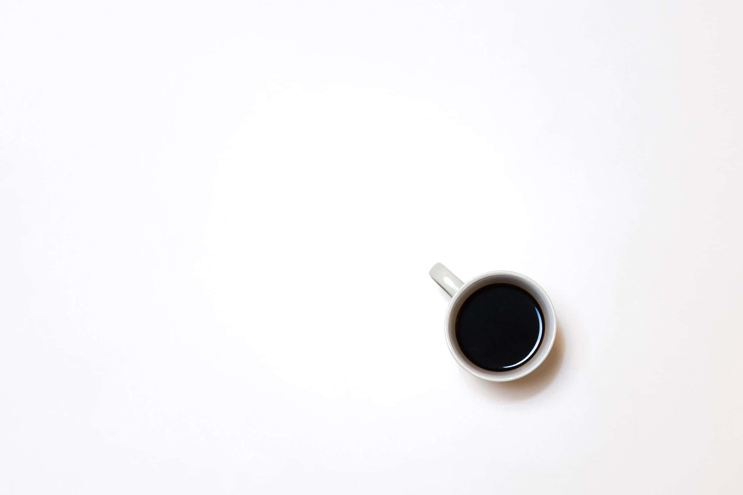 Minimalist Coffee 桌布 壁紙 — 一個簡約風格的白色馬克杯裝滿黑咖啡，置於明亮的白色表面上。