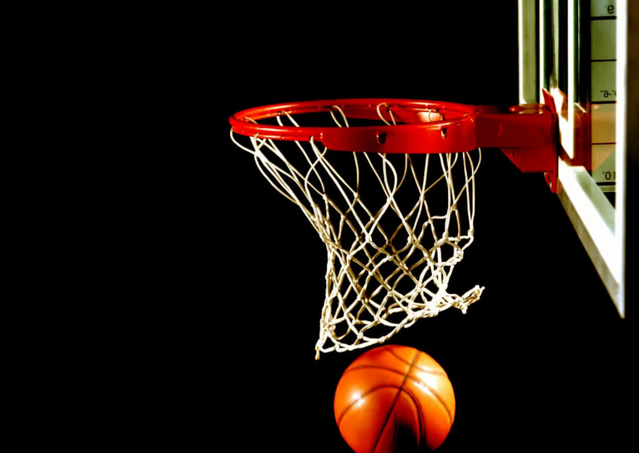Cool Basketball 桌布 壁紙 — 一個籃球懸掛在紅色籃框正下方，背景為純黑色，帶有戲劇性燈光。