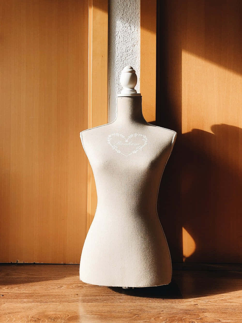 Clothing Design 桌布 壁紙 — 一個米色人體模型站在溫暖的陽光下，在木地板和牆壁上投下長長的陰影。