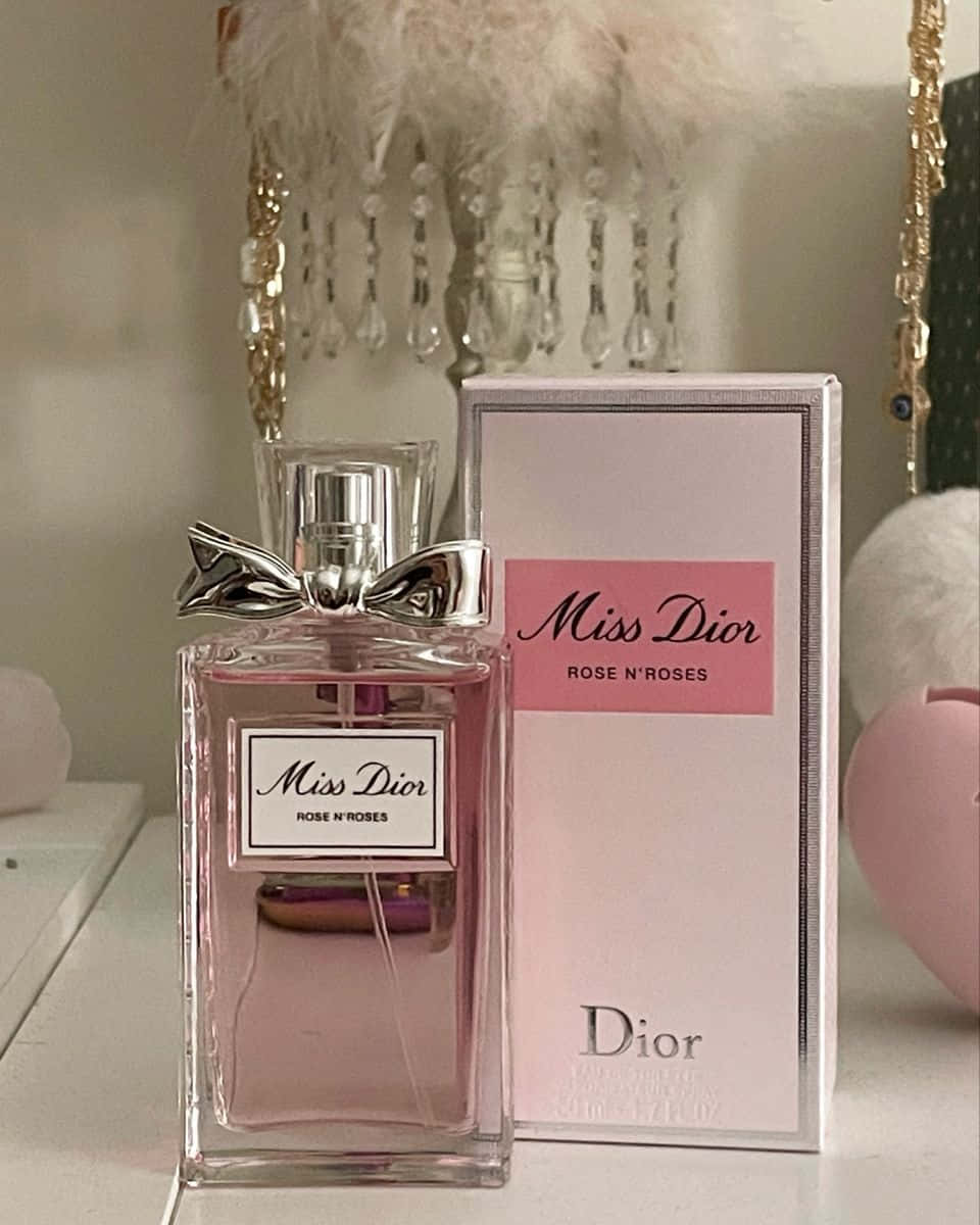 Rose Oil 桌布 壁紙 — 一個粉紅色嘅 Miss Dior 香水樽，帶有銀色蝴蝶結，擺喺白色架上面，旁邊係佢嘅盒，仲有 fluffy 粉紅色裝飾。