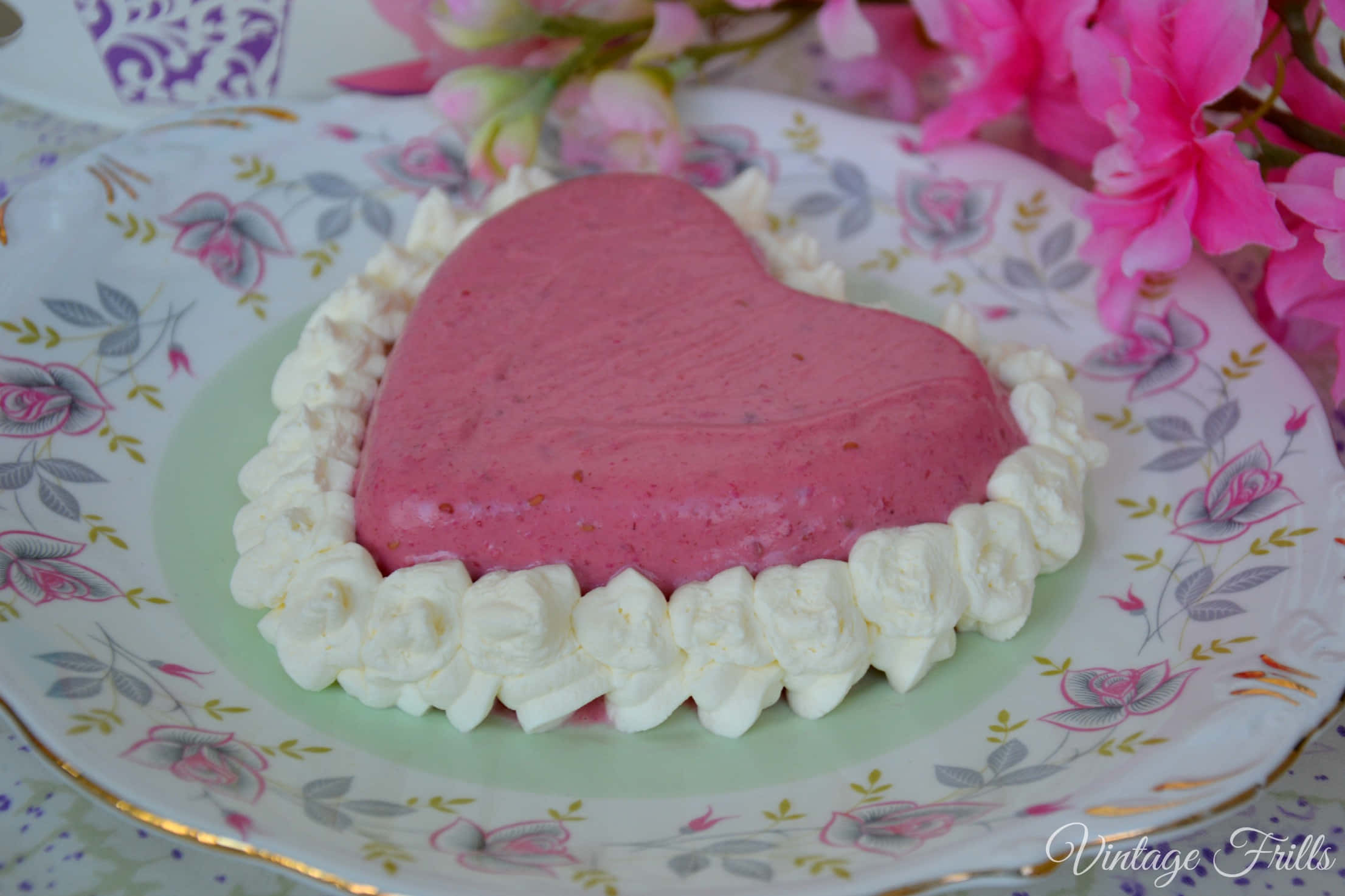 Blancmange 桌布 壁紙 — 一個粉紅色心形啫喱甜品，上面唧有忌廉，放在一個花卉圖案的碟子上，旁邊有粉紅色的花朵。