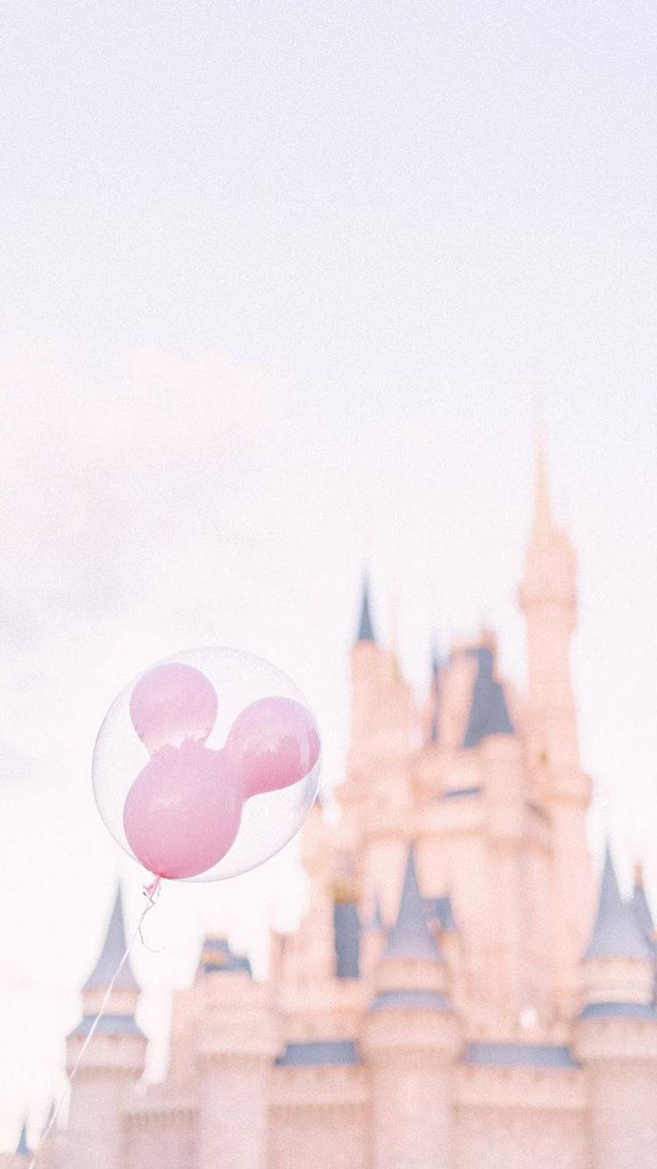 Disneyland Castle 桌布 壁紙 — 一個粉紅色米奇老鼠氣球在朦朧的天空下，輕輕飄浮在柔焦的迪士尼城堡前。