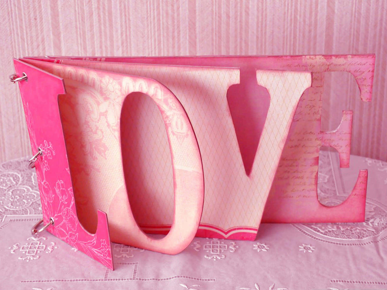 3d Love 桌布 壁紙 — 一個粉紅色紙剪字 LOVE 打開放在蕾絲枱布上，背景是條紋牆紙。