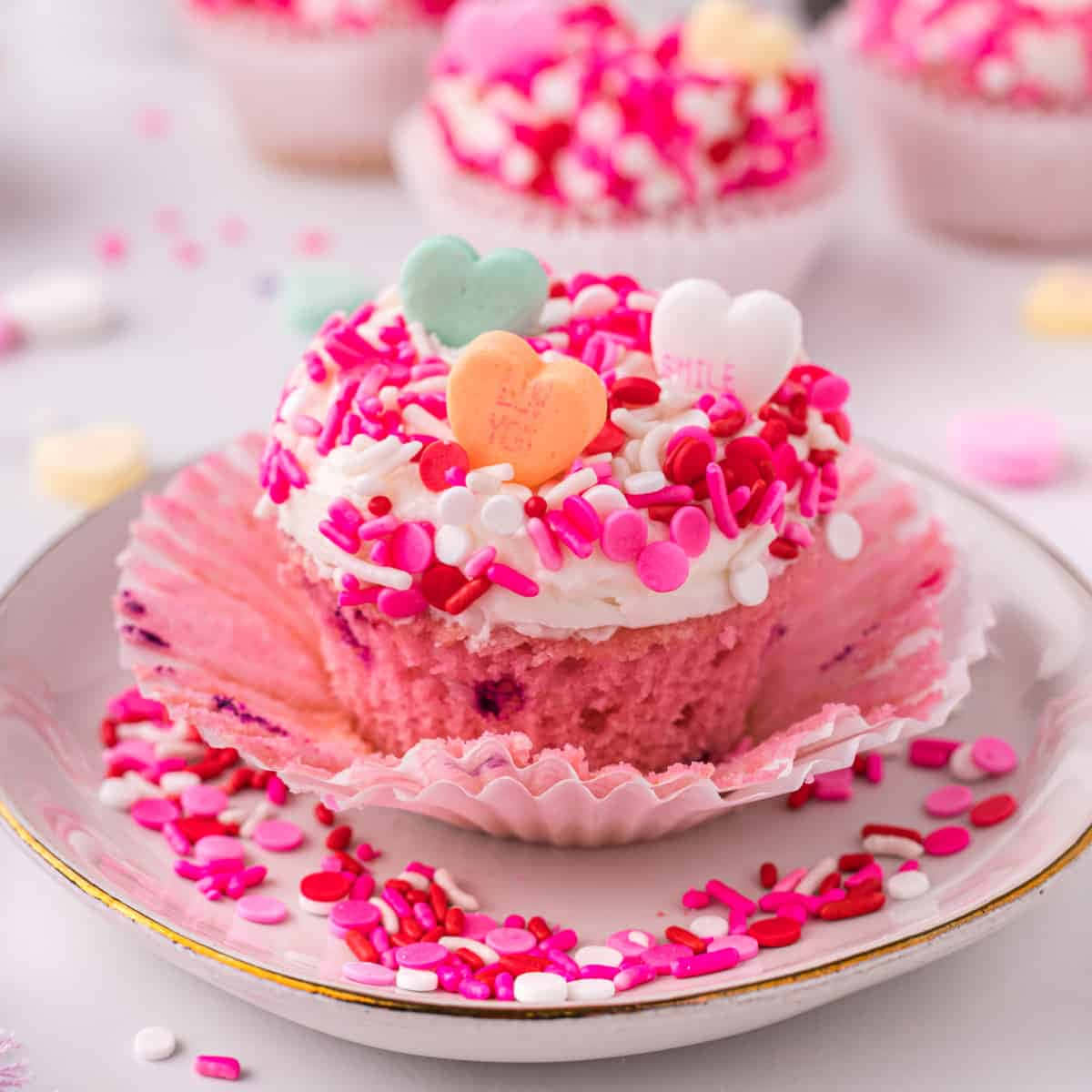 Pink Cupcakes 桌布 壁紙 — 一個粉紅色紙杯蛋糕的特寫，上面有白色糖霜和色彩繽紛的心形糖粒，放在裝飾盤上。