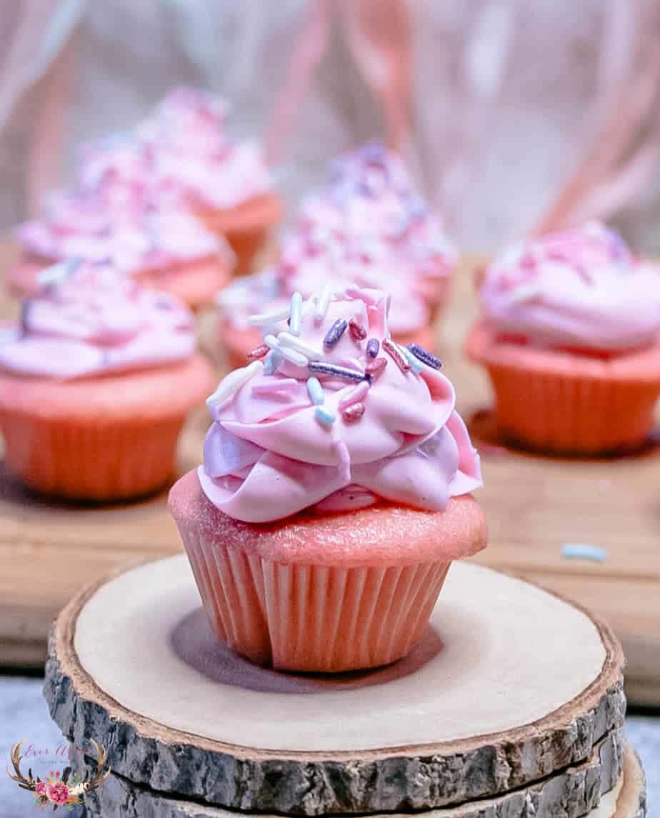 Pink Cupcakes 桌布 壁紙 — 一個粉紅色紙杯蛋糕的特寫，上面有漩渦狀的糖霜和彩色糖粒，放在一塊鄉村風格的木片上。