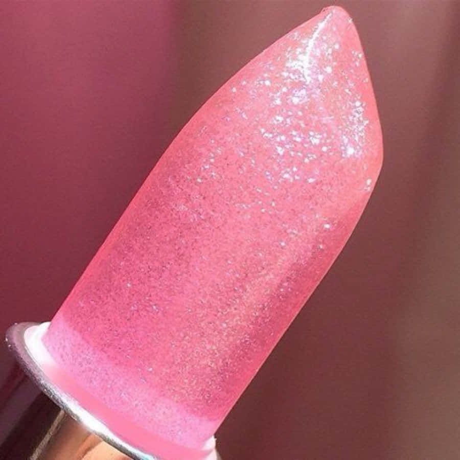 Pink Lipstick 桌布 壁紙 — 一個粉紅色閃粉唇膏的特寫，帶有金屬蓋，背景是模糊的栗色。