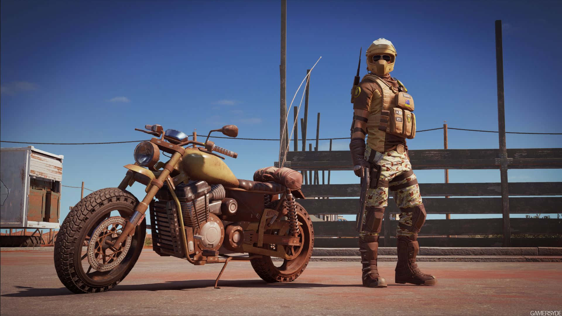 Rainbow Six Siege Mozzie 桌布 壁紙 — 一個粗獷的沙漠戰士站在一輛飽經風霜的電單車旁，背景是晴朗的藍天和木柵欄。