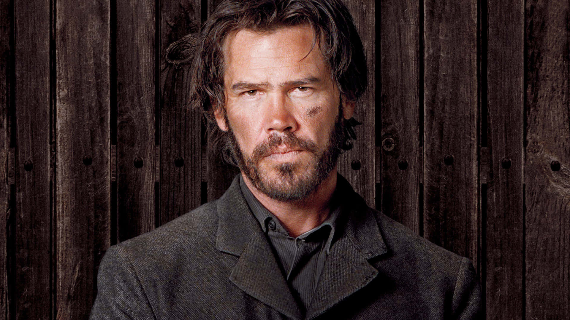 Josh Brolin 桌布 壁紙 — 一個粗獷的男人，留著鬍鬚，臉上沾滿泥土，凝視著風化的木牆。