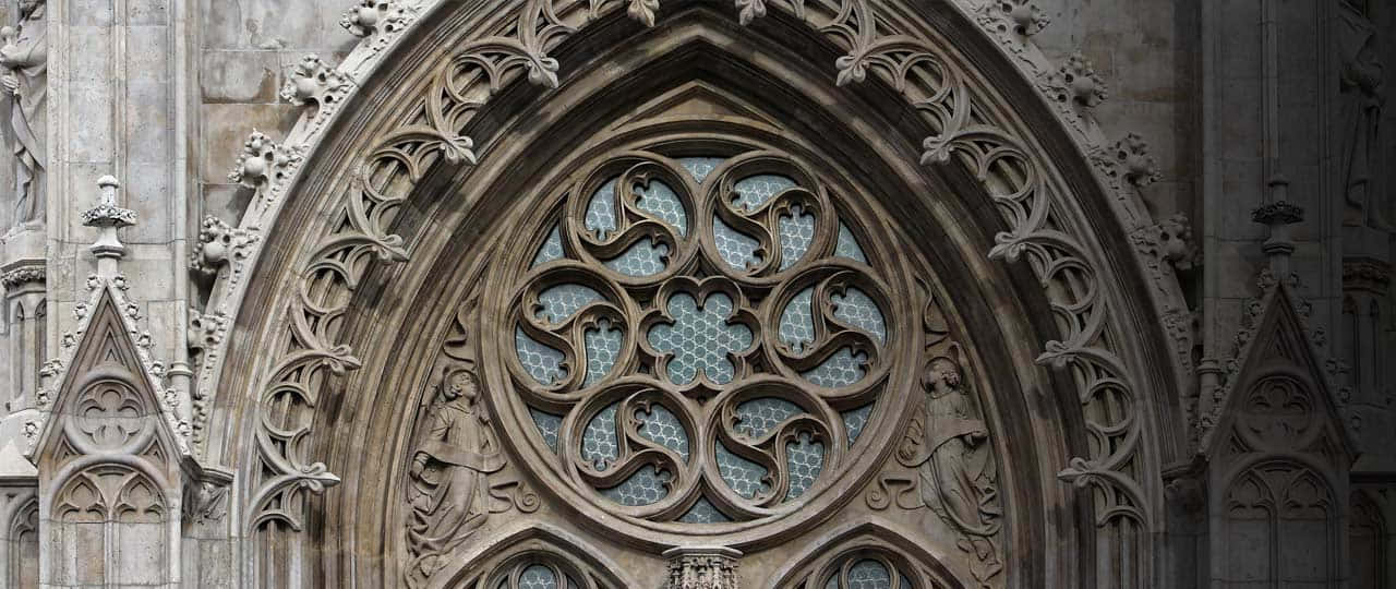 Gothic Architecture 桌布 壁紙 — 一個精緻的石造哥德式玫瑰窗，帶有詳細的窗飾和雕像，設置在風化的教堂外牆上。
