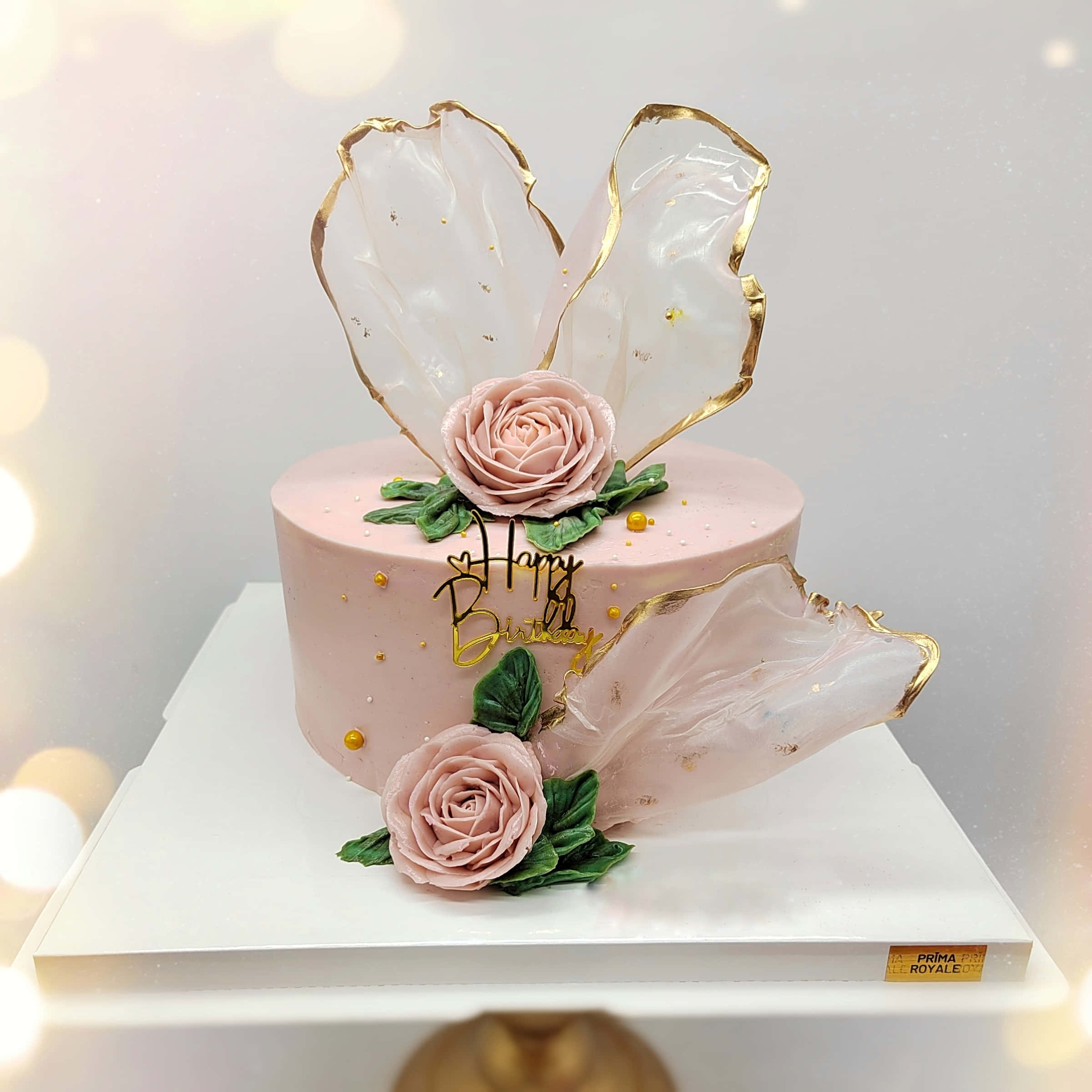 Floral Cake 桌布 壁紙 — 一個精緻的粉紅色生日蛋糕，飾有糖玫瑰、金箔點綴和半透明翅膀，放在白色底座上。