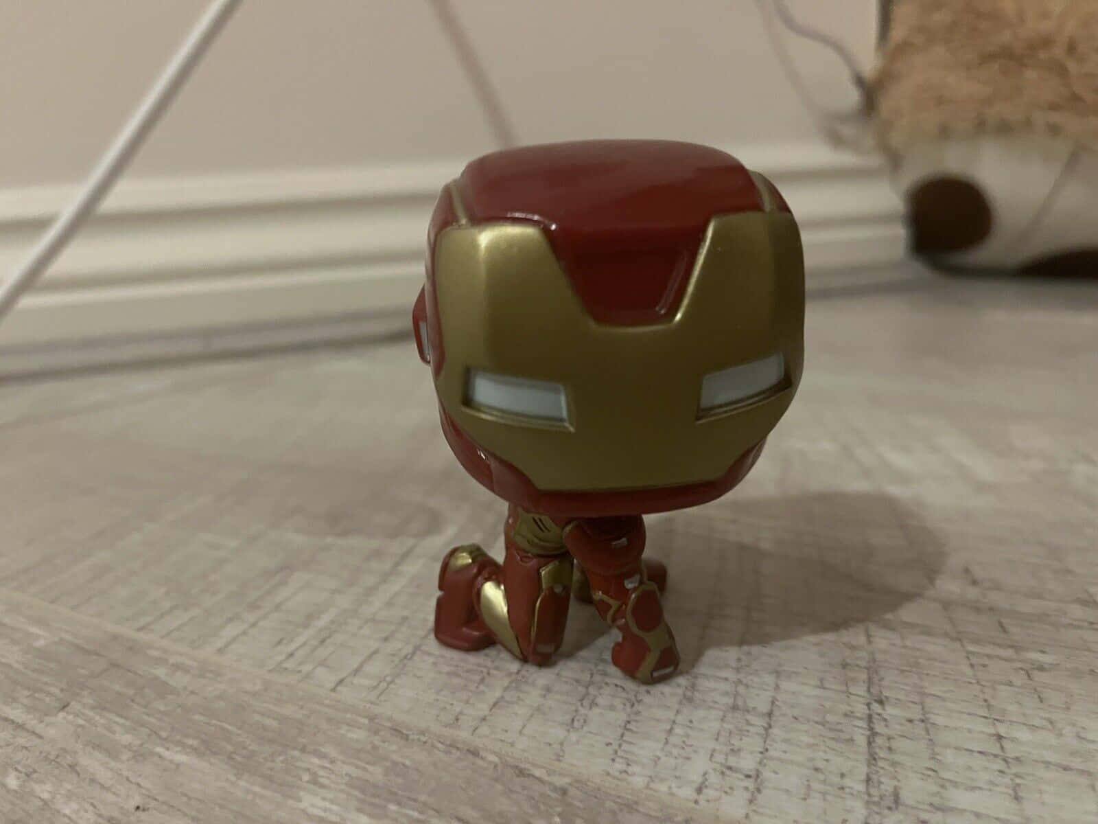 Iron Man Pop Figures 桌布 壁紙 — 一個紅色和金色的鐵甲奇俠 Funko Pop! 人偶跪在淺色木地板上，背景模糊。
