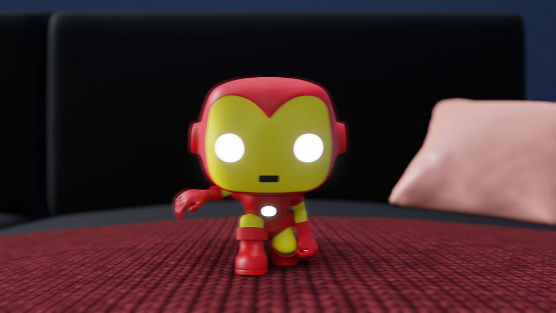 Iron Man Pop Figures 桌布 壁紙 — 一個紅色和金色的鐵甲奇俠Funko Pop!人偶站在有紋理的紅色表面上，眼睛發光，背景有黑色沙發。