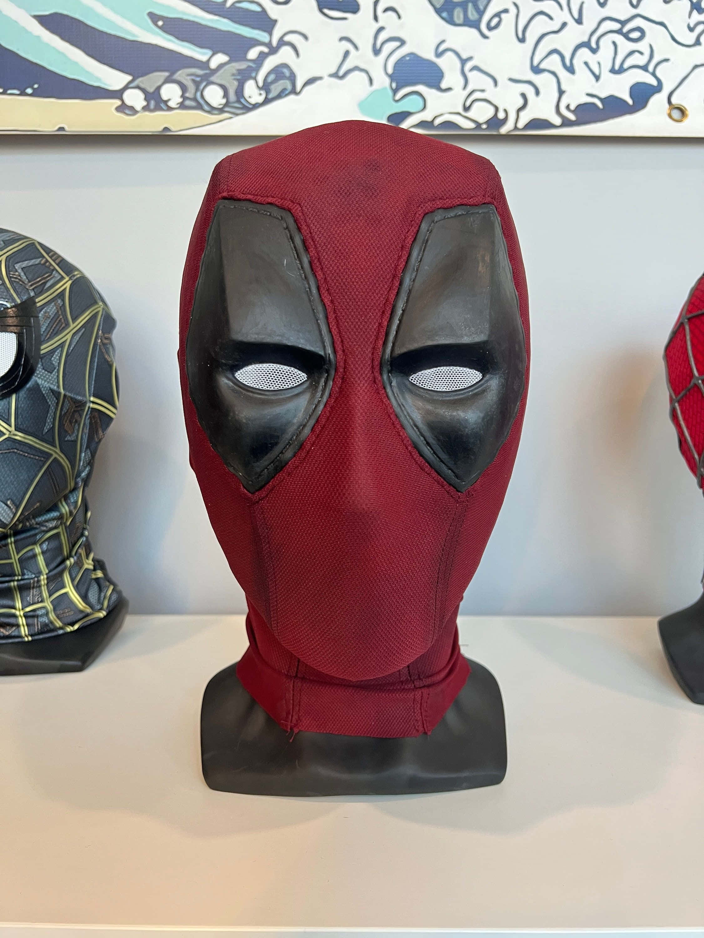 Deadpool Mask 桌布 壁紙 — 一個紅色和黑色的死侍面具陳列在架上的展示架上，與其他超級英雄面具一起。