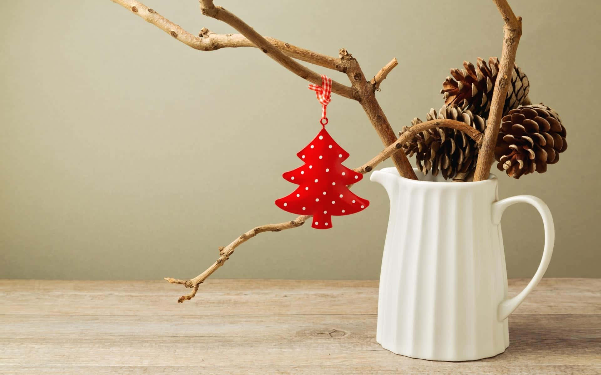 Rustic Christmas 桌布 壁紙 — 一個紅色圓點聖誕樹裝飾品掛在一根帶有松果的裸露樹枝上，放在木桌上的白色陶瓷壺裡。