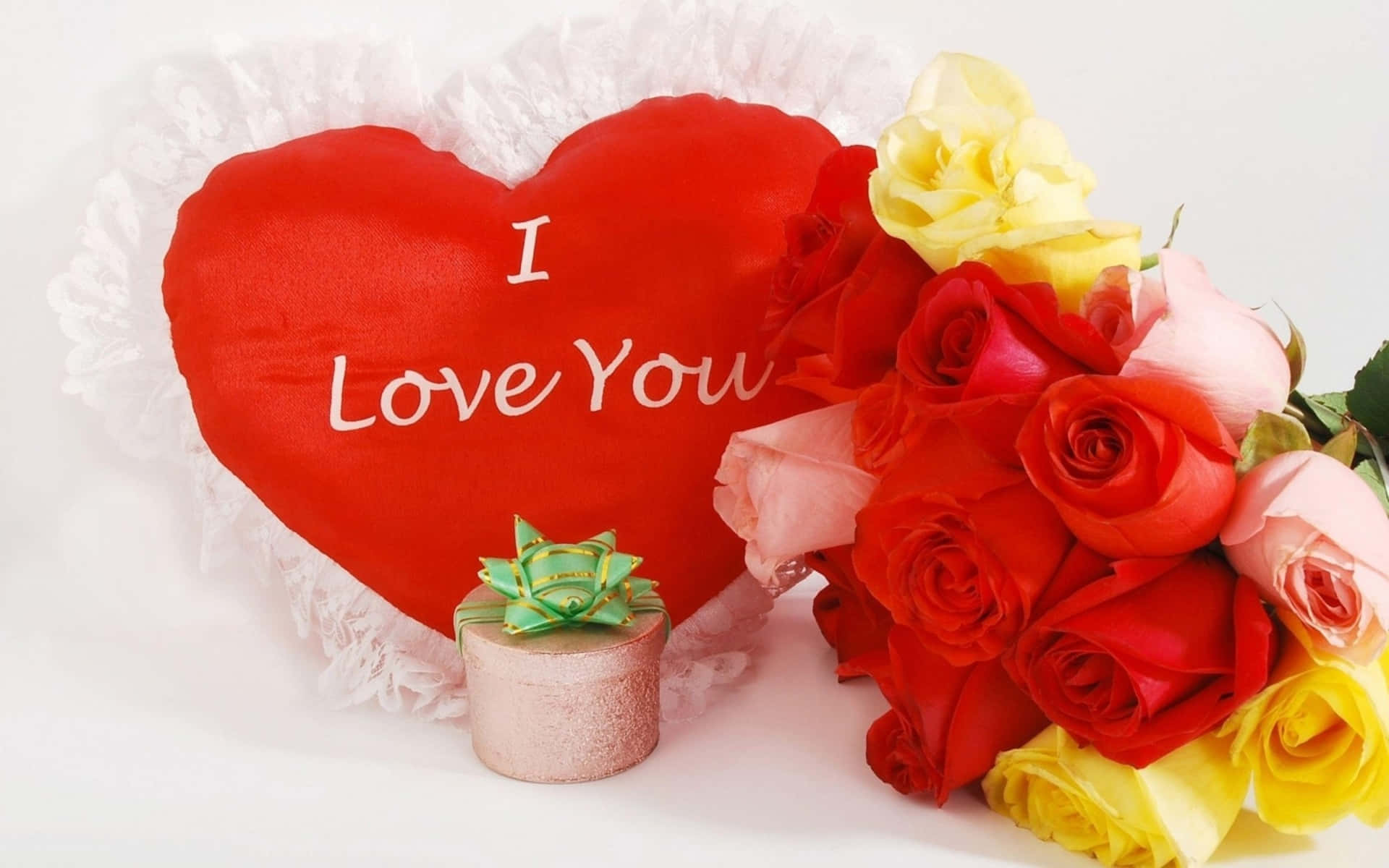  壁紙 — 一個紅色心形枕頭，上面有 I Love You 字樣，旁邊放著一束紅、粉紅和黃色的玫瑰，以及一個小禮物盒。