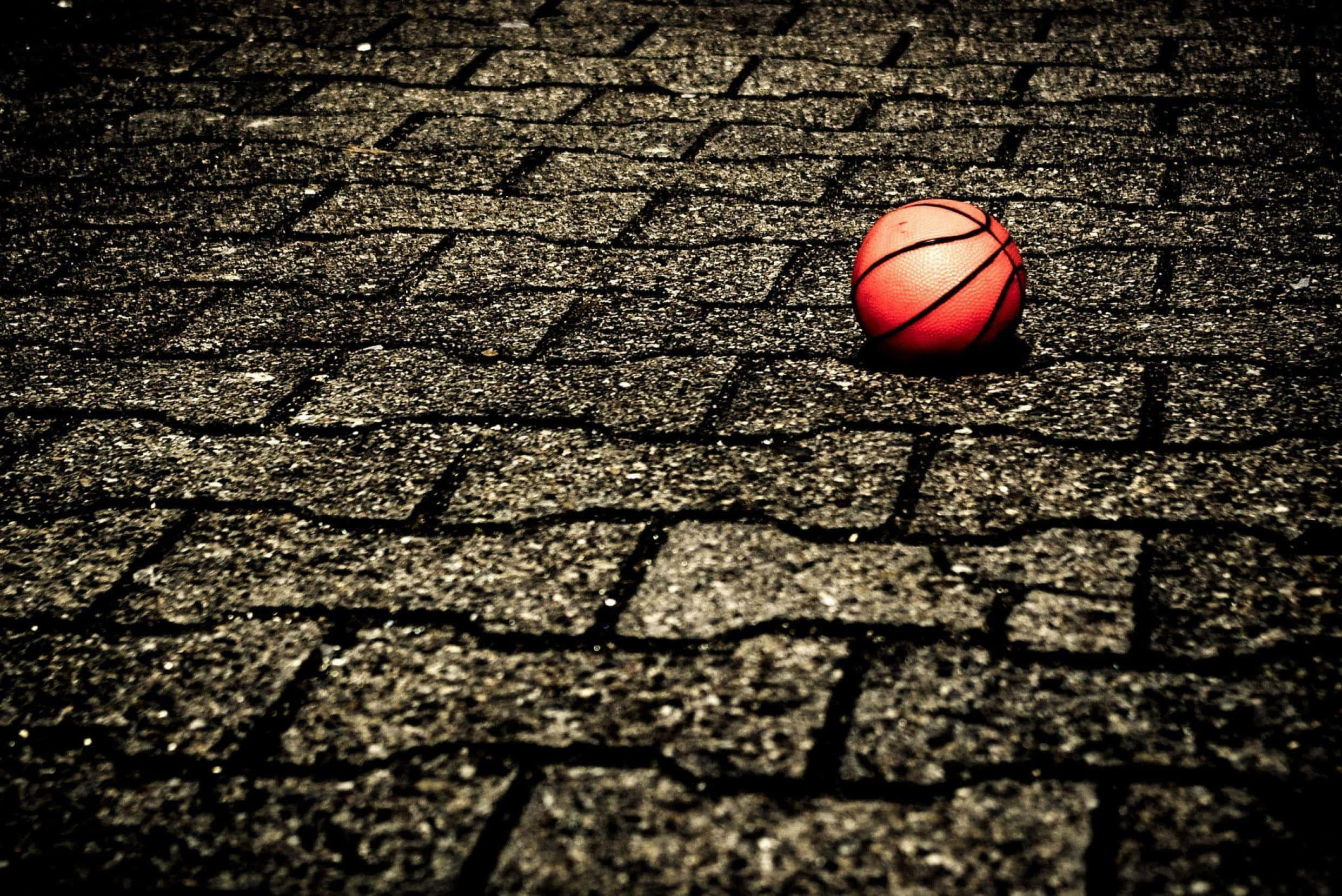 Cool Basketball 桌布 壁紙 — 一個紅色籃球放在裂開的瀝青球場上，在戲劇性的低角度燈光下。