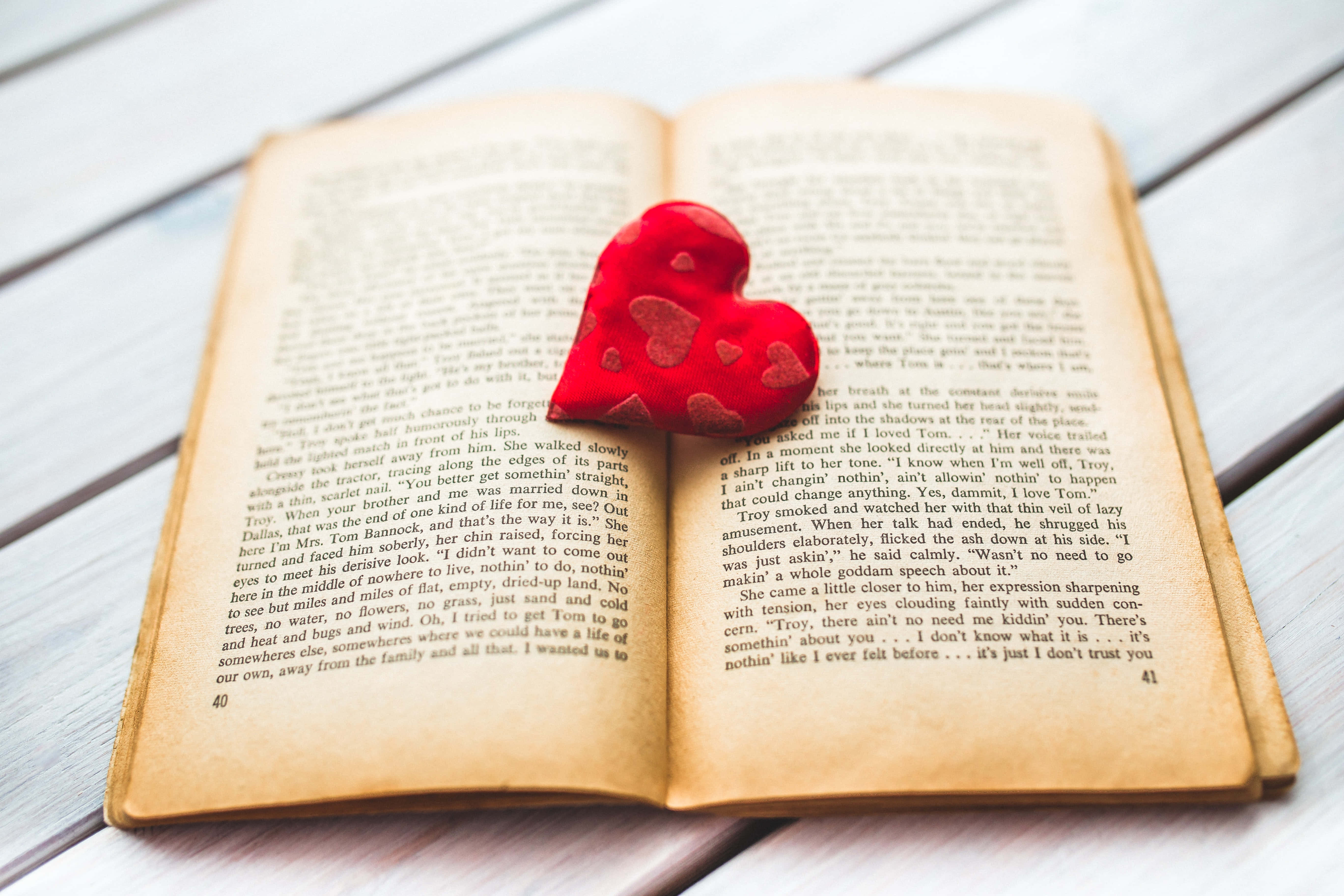Romance Literature 桌布 壁紙 — 一個紅色紋理的心形放在打開的書頁上，書頁上有可見的文字和頁碼。