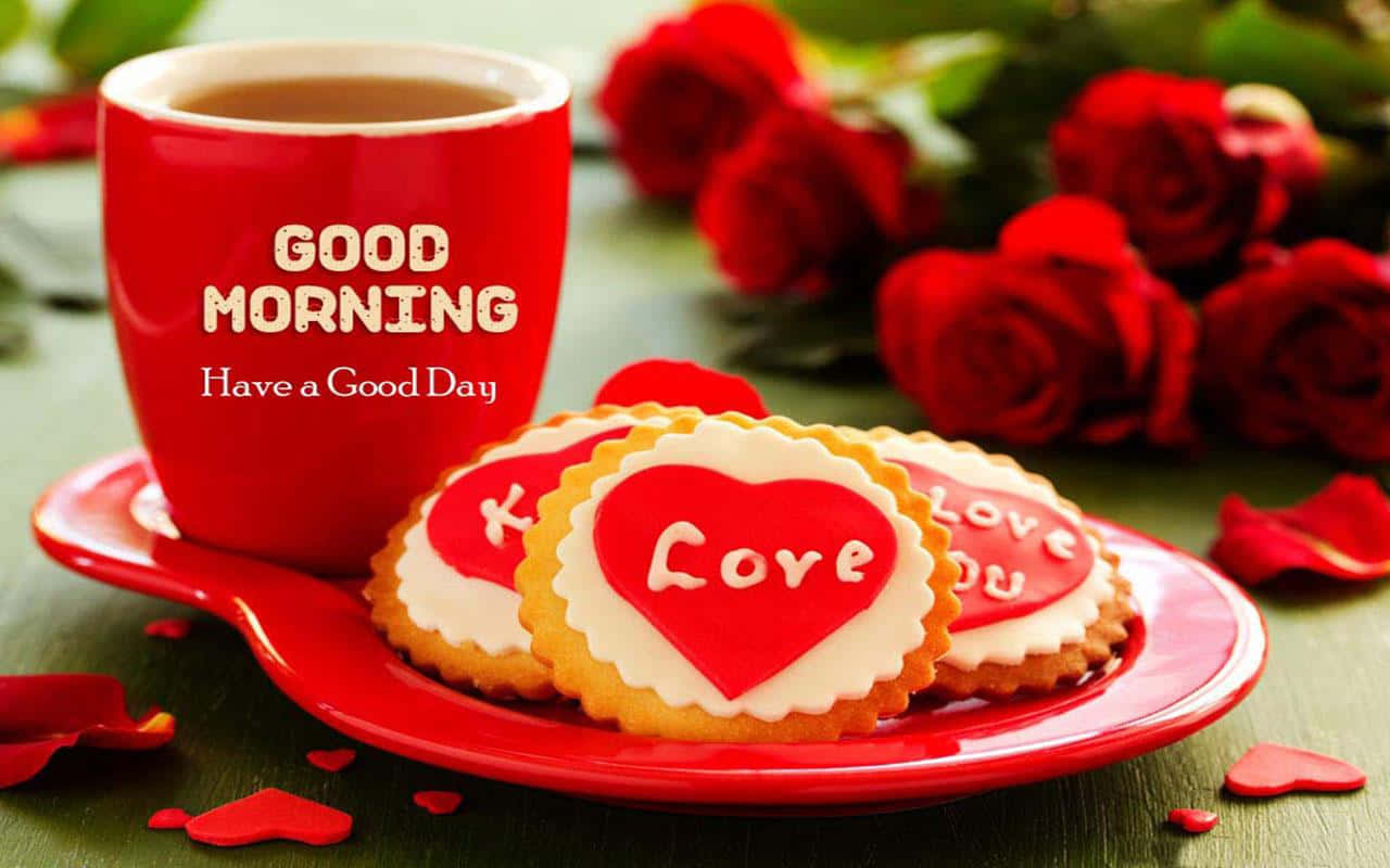 壁紙 — 一個紅色馬克杯上寫著 'GOOD MORNING'，旁邊有心形曲奇和新鮮紅玫瑰，放在綠色木桌上。