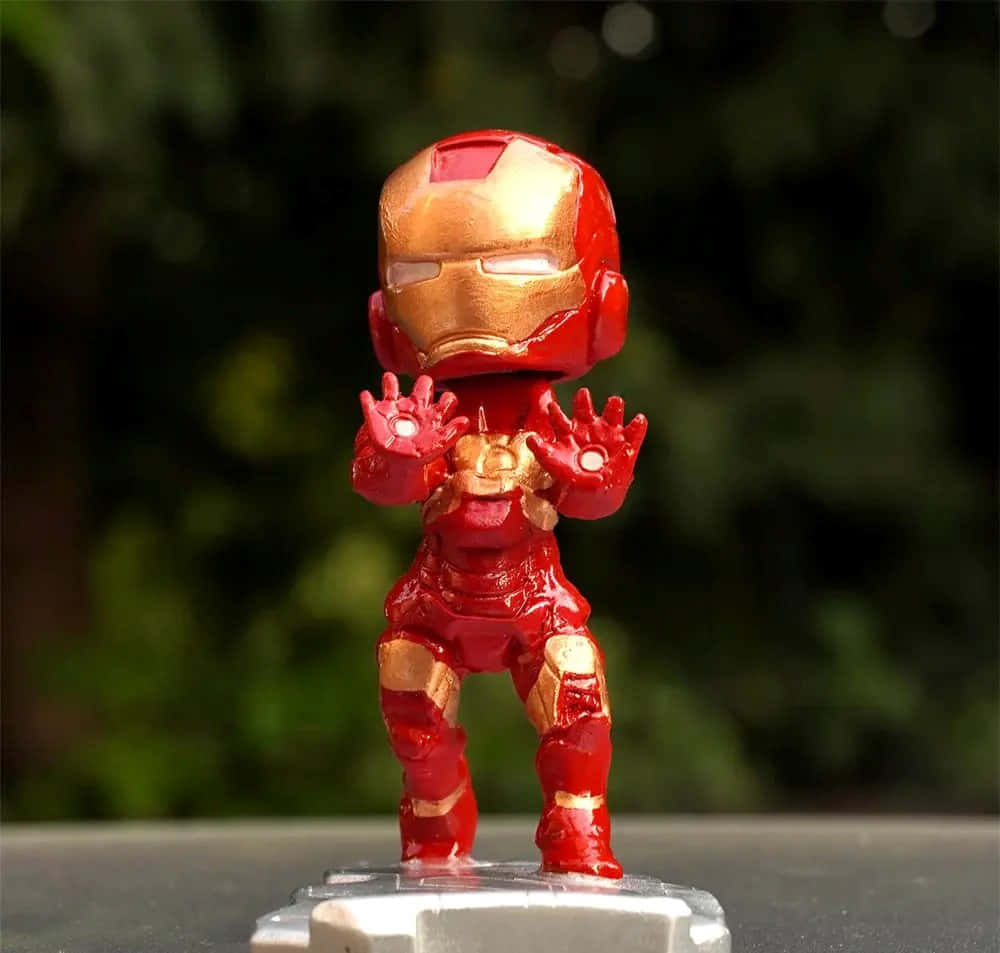 Iron Man Bobbleheads 桌布 壁紙 — 一個紅金色的Q版鐵甲奇俠人偶，站在透明底座上，雙手發出光芒，背景是模糊的綠色。