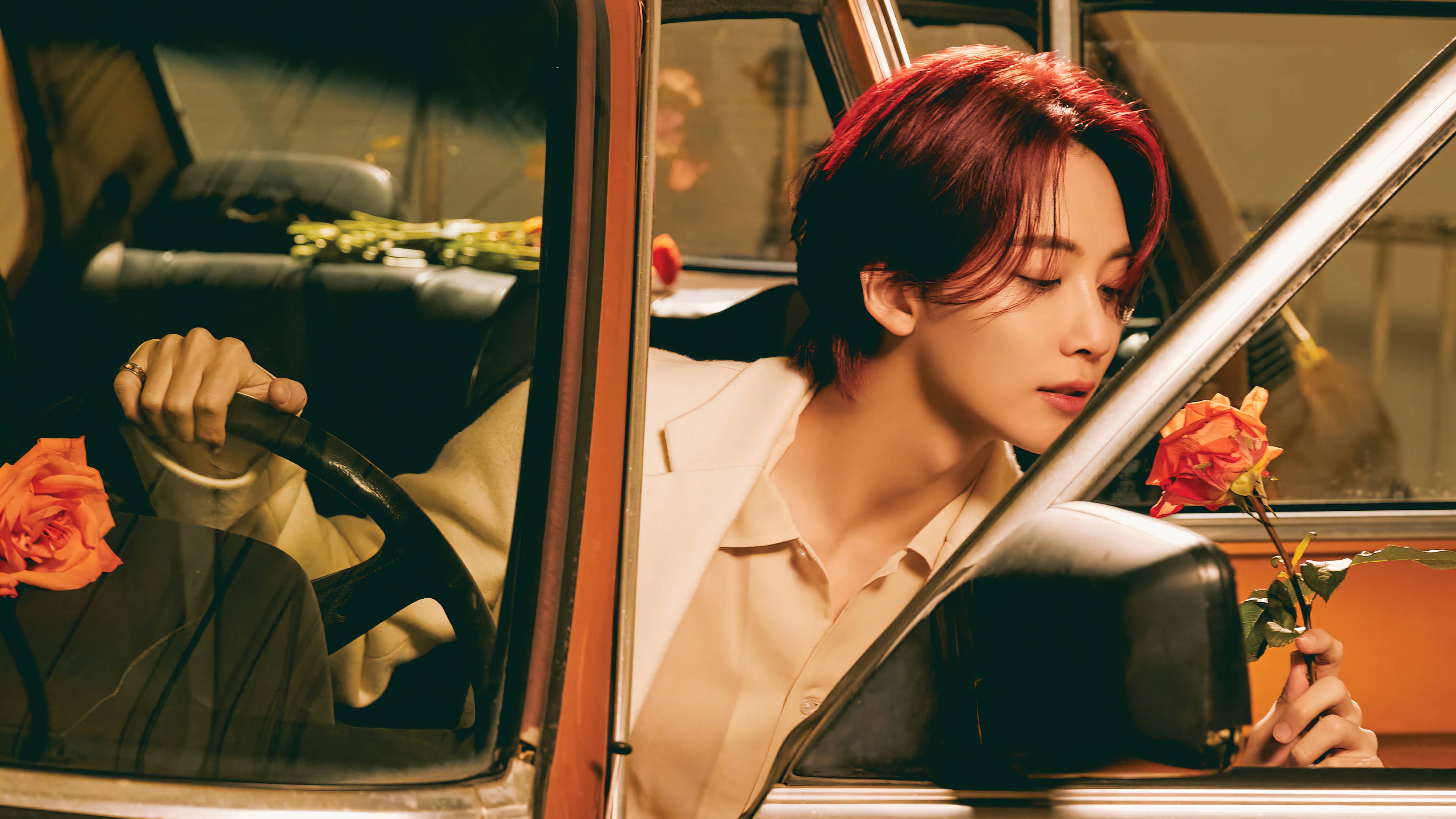Yoon Jeonghan Your Choice 壁紙 — 一個紅髮的人坐在一輛復古車裏，手持一朵玫瑰，沐浴在溫暖的金色光線中。