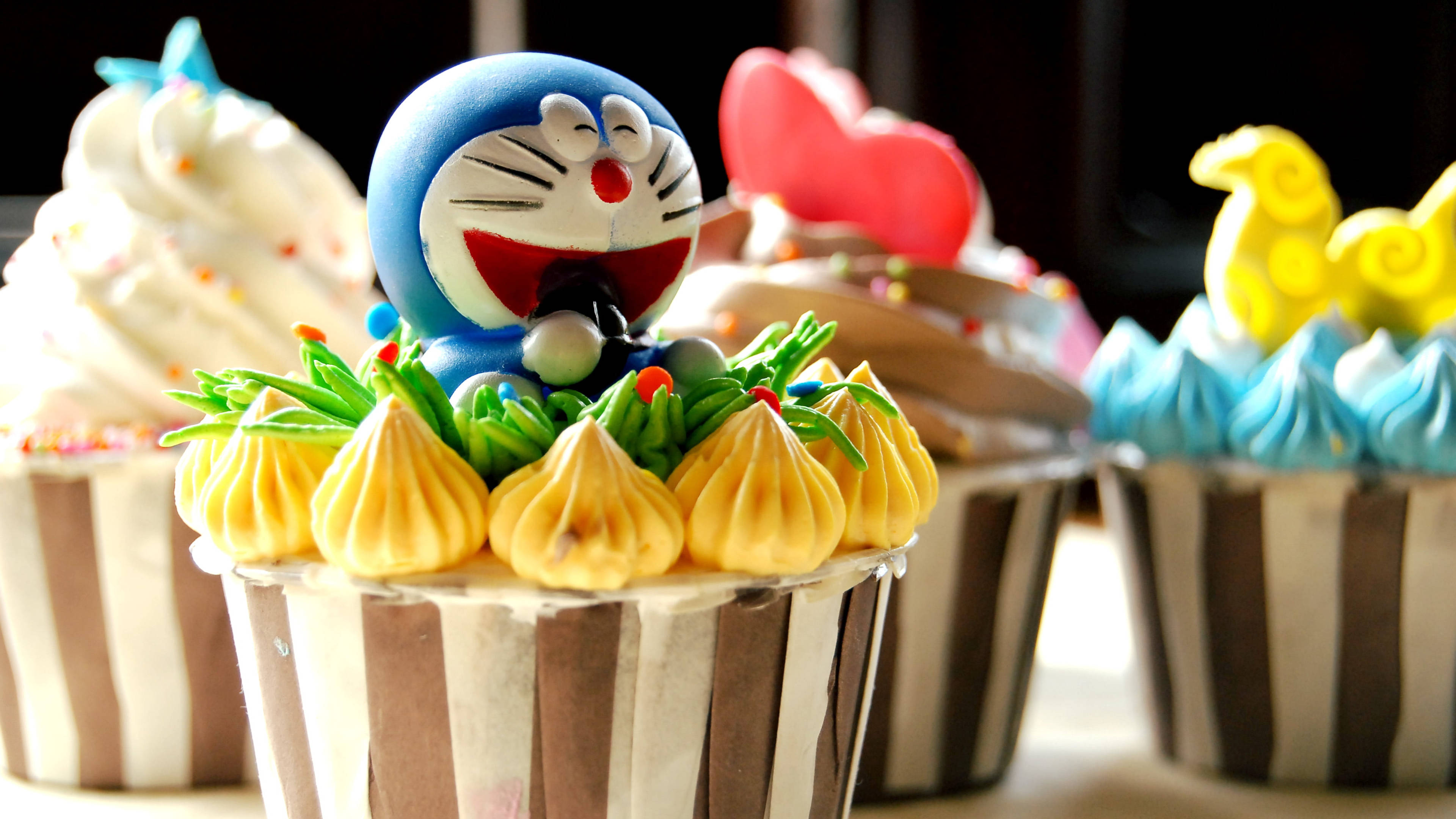 Doraemon 桌布 壁紙 — 一個紙杯蛋糕的特寫，上面放著一個微笑的藍色多啦A夢公仔，周圍環繞著擠花黃色糖霜。