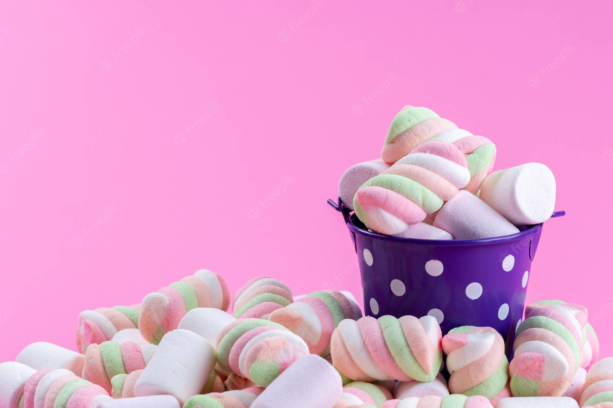 Marshmallow 桌布 壁紙 — 一個紫色圓點桶，裝滿了粉彩漩渦棉花糖，背景是充滿活力的粉紅色。