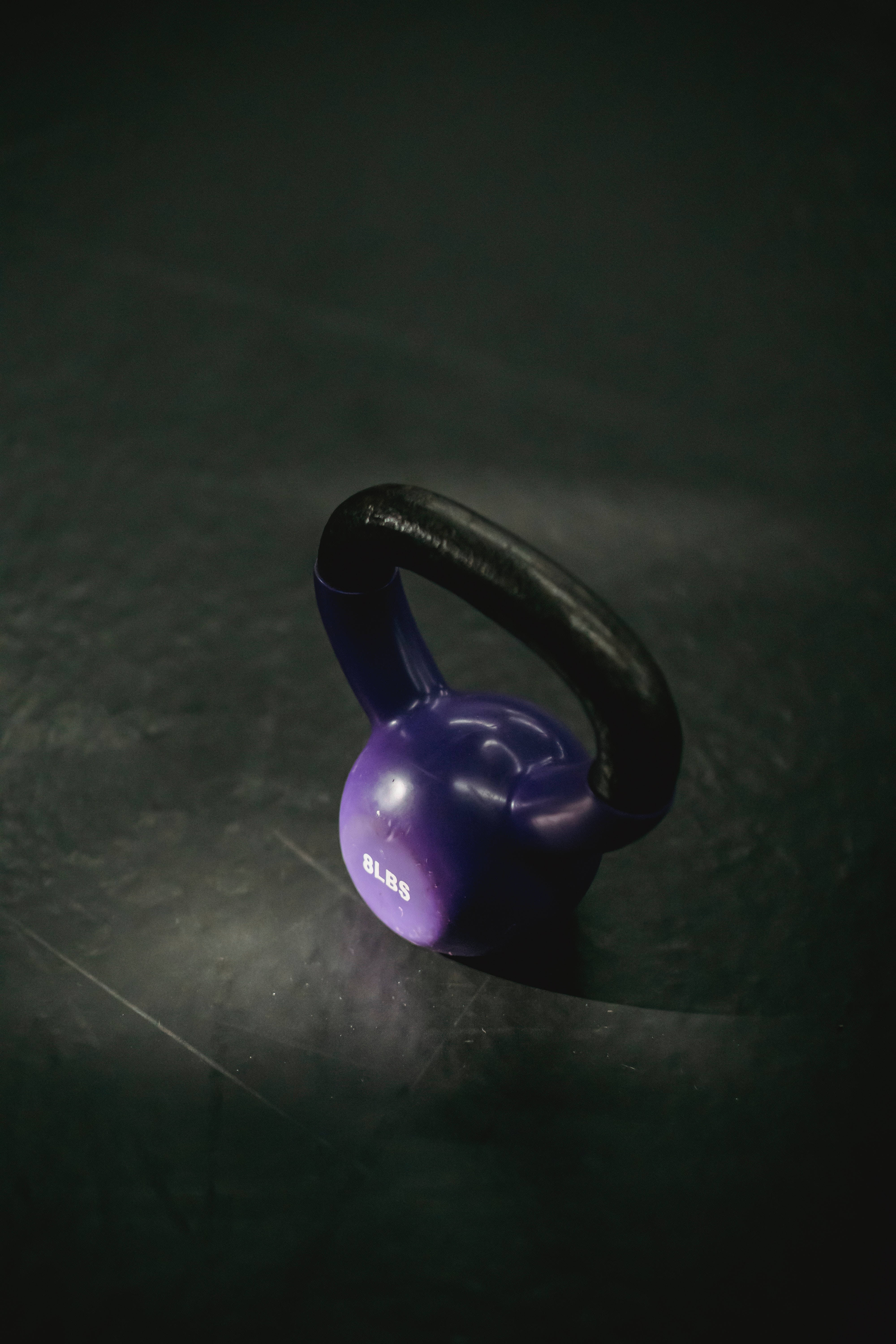 Black And Purple Phone 桌布 壁紙 — 一個紫色的8磅壺鈴放在黑暗的健身房地板上，在戲劇性的聚光燈下。
