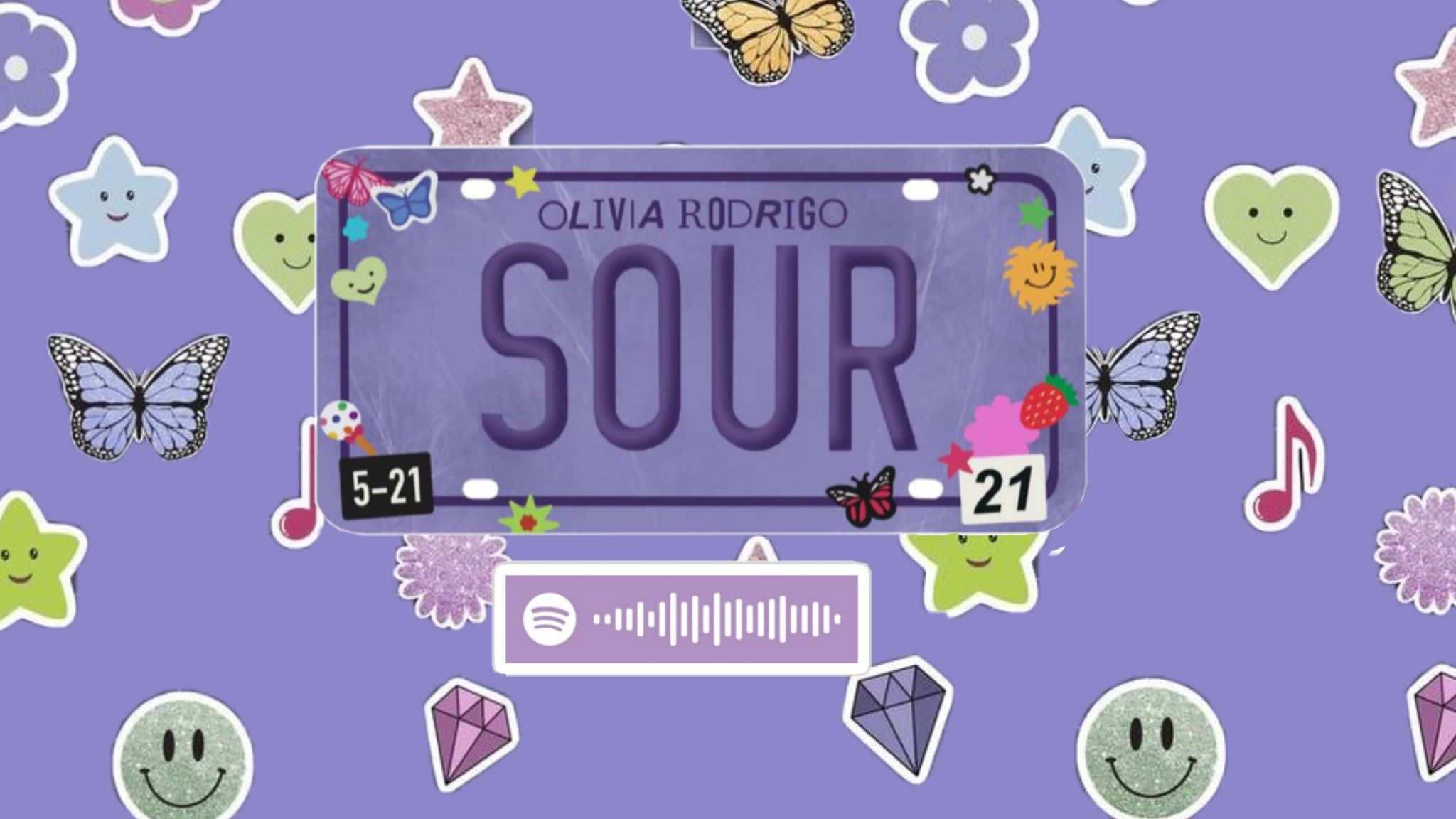 Olivia Rodrigo 桌布 壁紙 — 一個紫色車牌，上面寫著 Olivia Rodrigo 的「SOUR」，周圍有色彩繽紛的蝴蝶、心形和音符貼紙，背景閃閃發光。